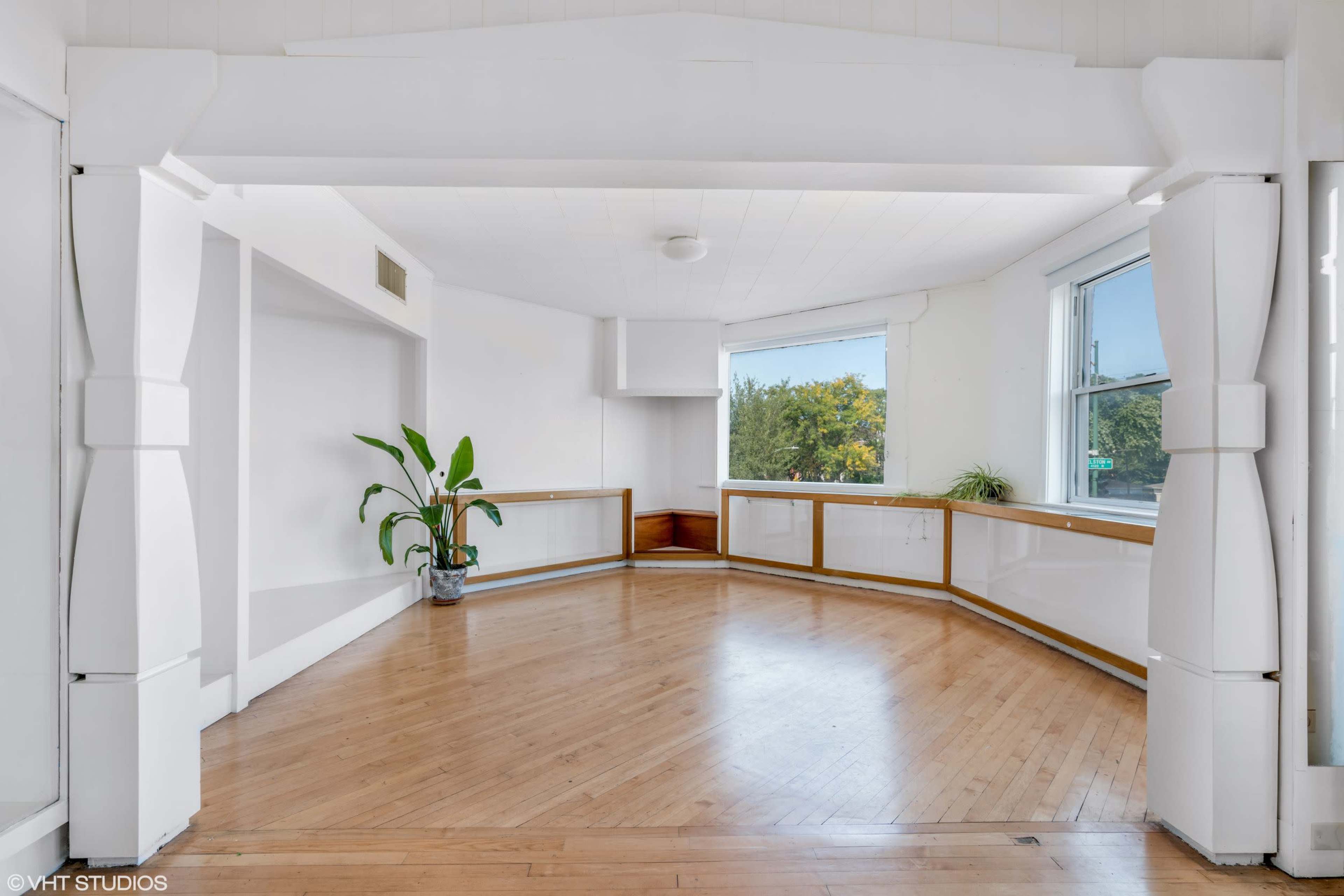 A spacious room features large windows, hardwood flooring, and a curved wall with built-in shelving.