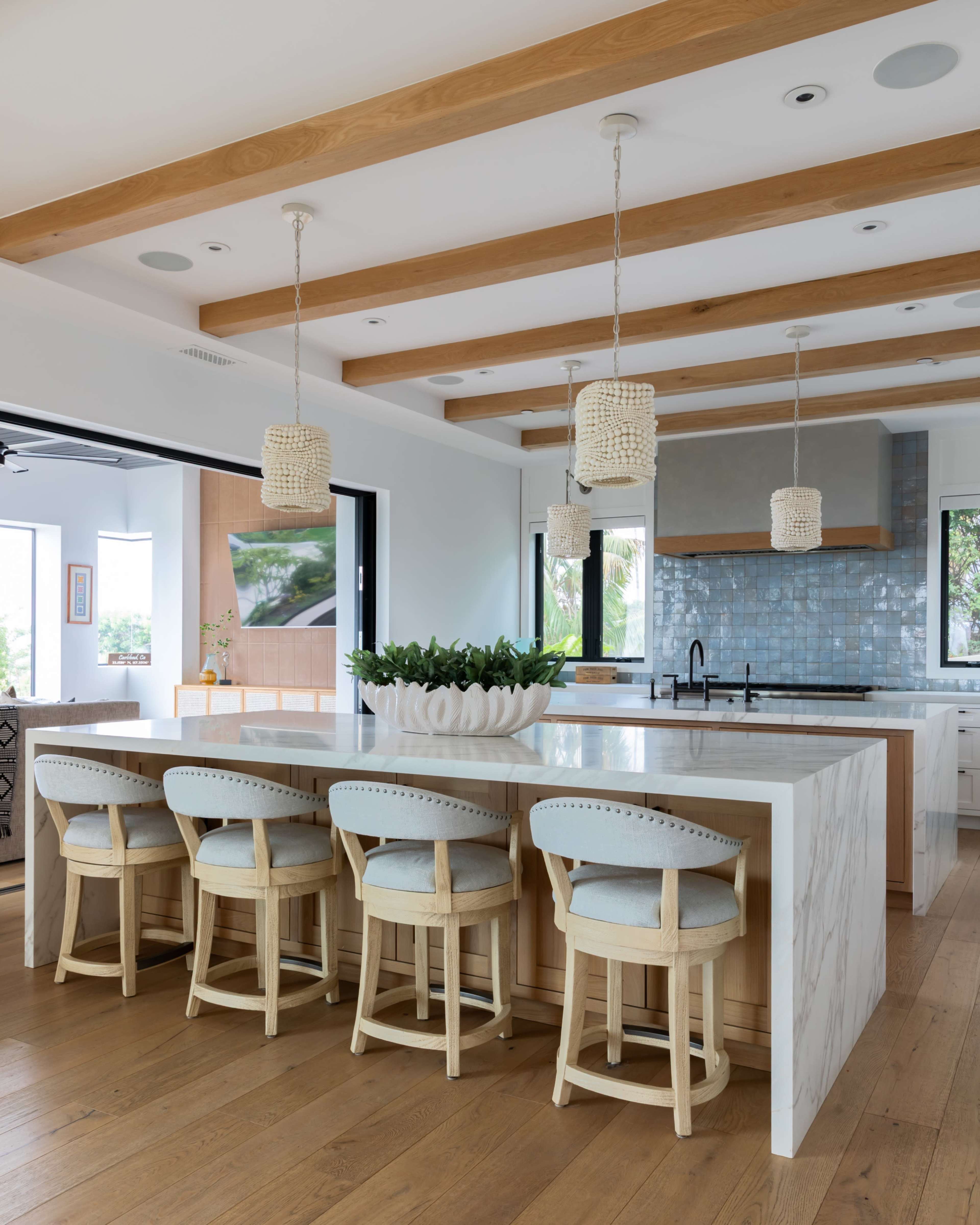 A modern kitchen features a large marble island with wooden bar stools and hanging pendant lights.