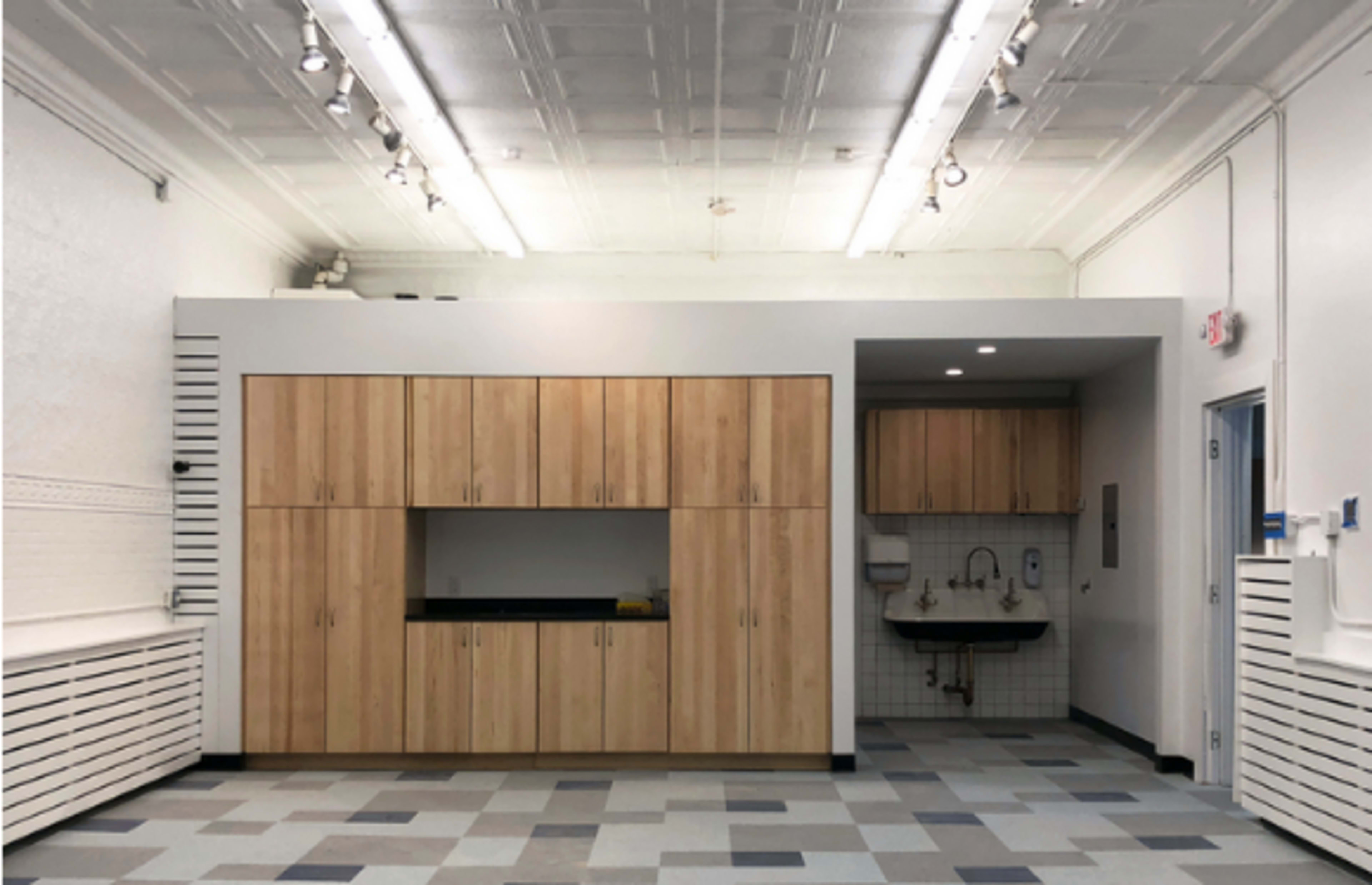 A spacious room with wooden cabinetry and a sink area, featuring a tiled backsplash and a patterned floor.