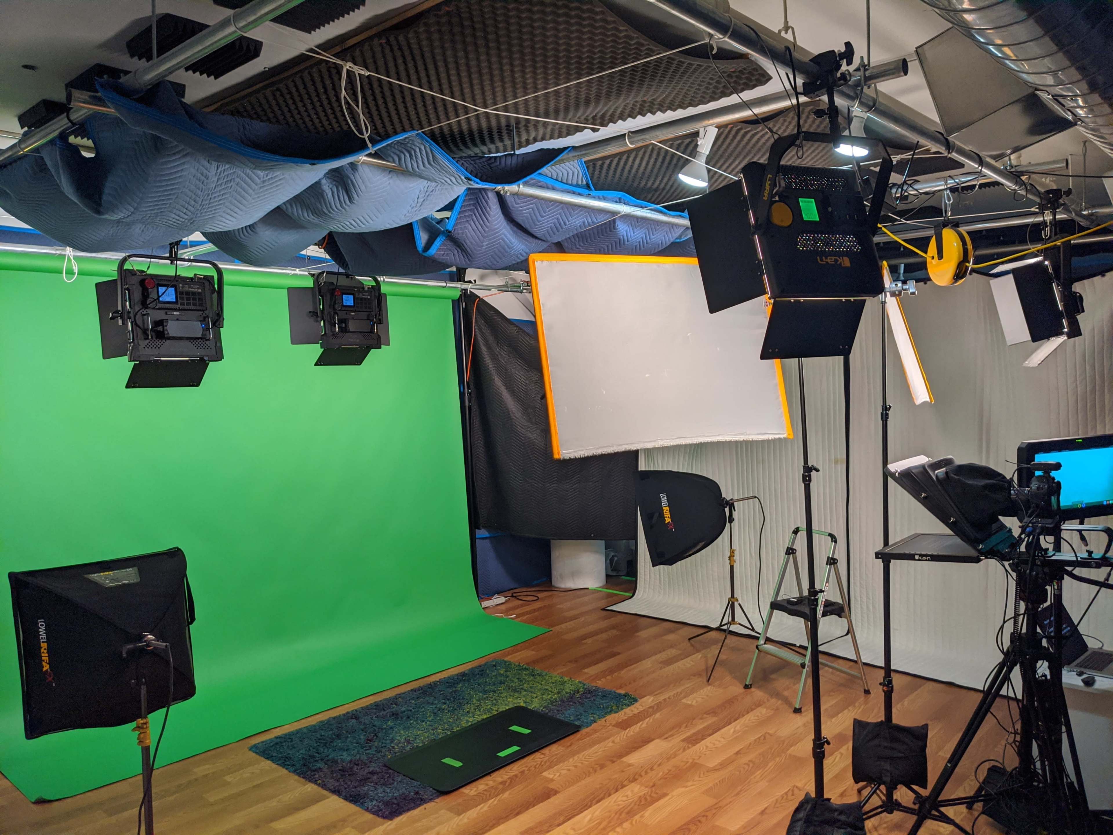 The image shows a studio setup with a green screen, various lighting equipment, and a camera on a tripod.