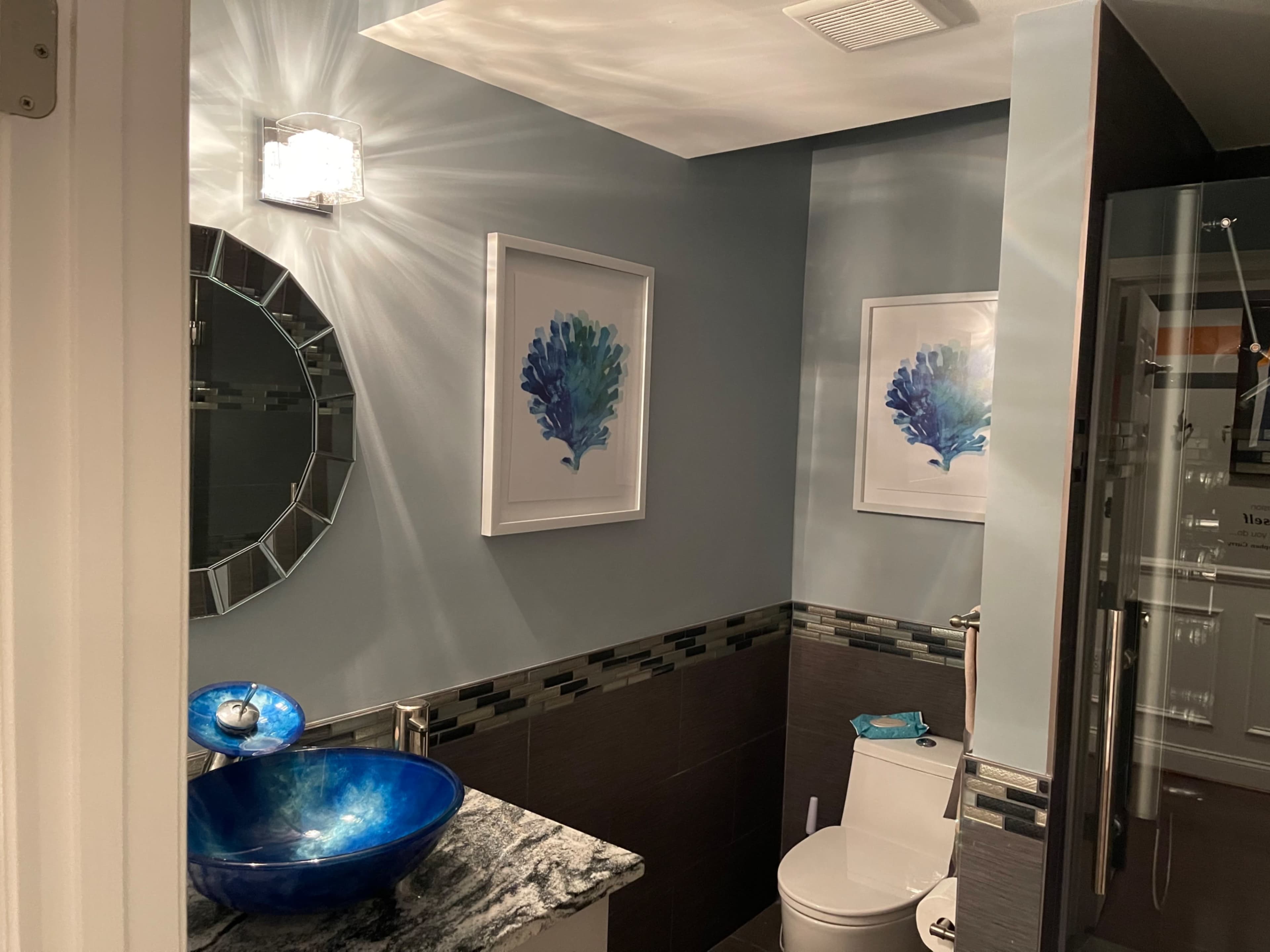 A bathroom featuring a round mirror, artistic wall prints, a blue sink, and a shower area.
