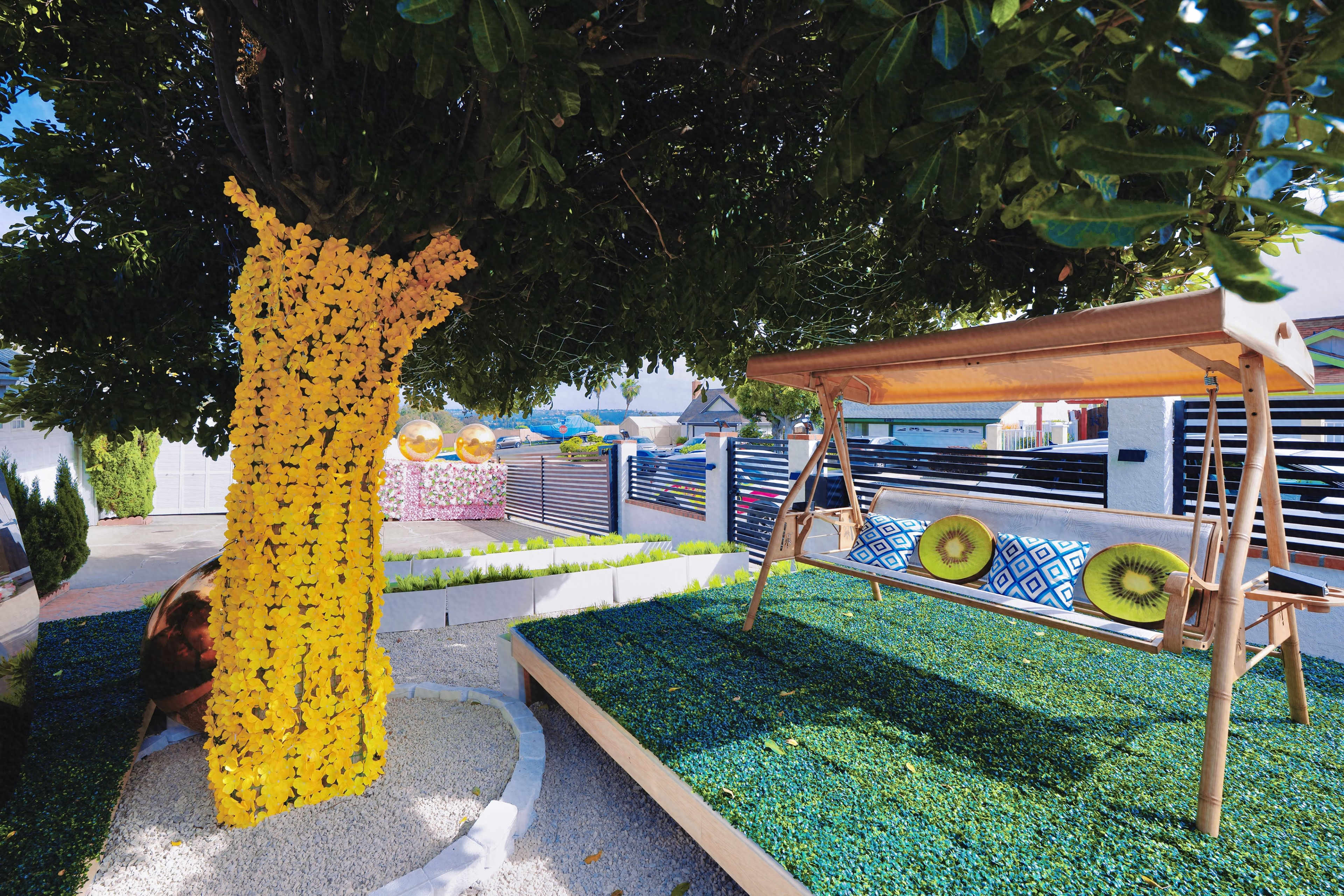 The image features a backyard landscape with a tree adorned in yellow flowers, a wooden swing, and vibrant green ground cover.