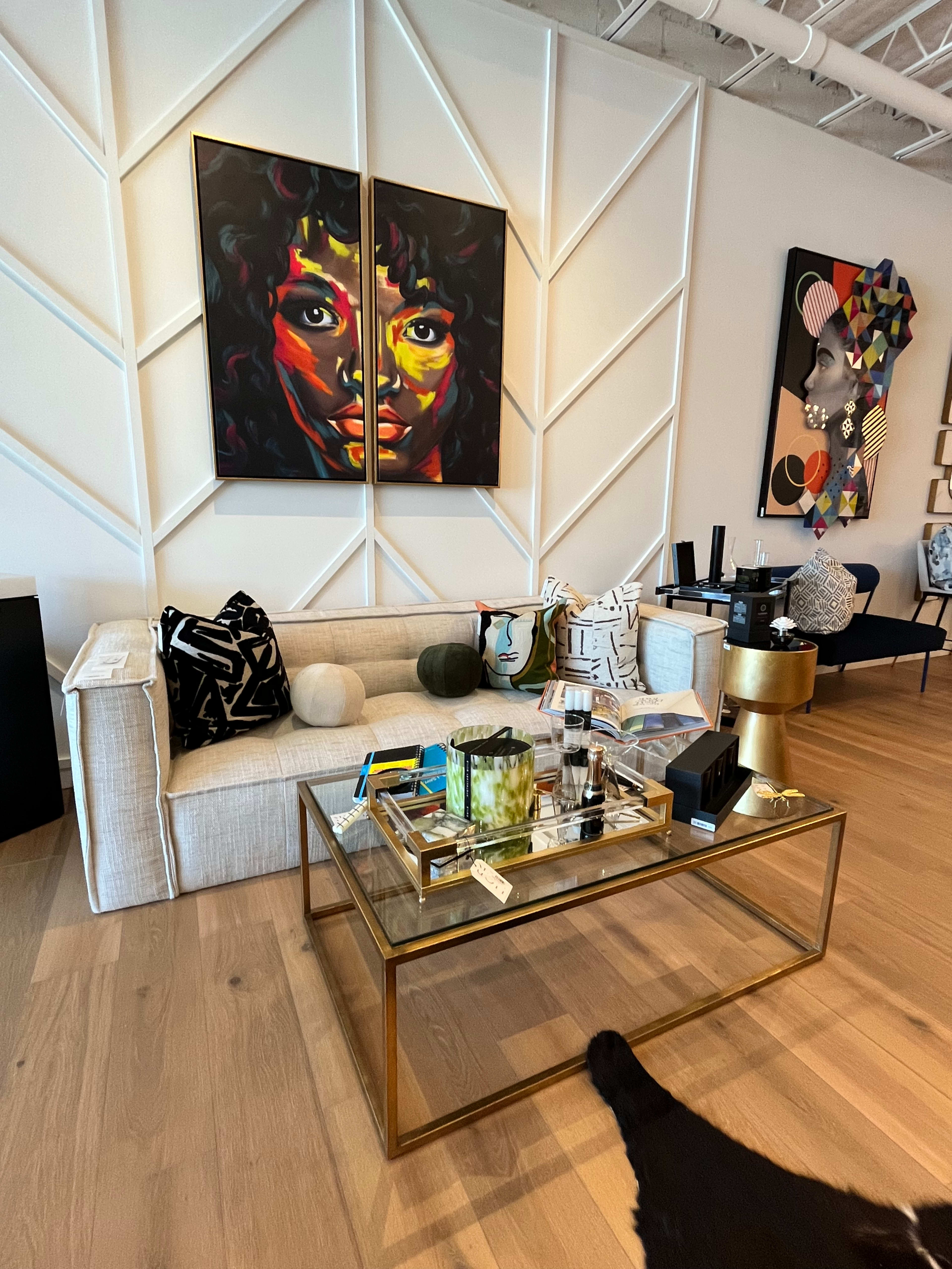 A stylish living room with a light-colored sofa, a gold-framed coffee table adorned with decorative items, and vibrant art pieces on the walls.