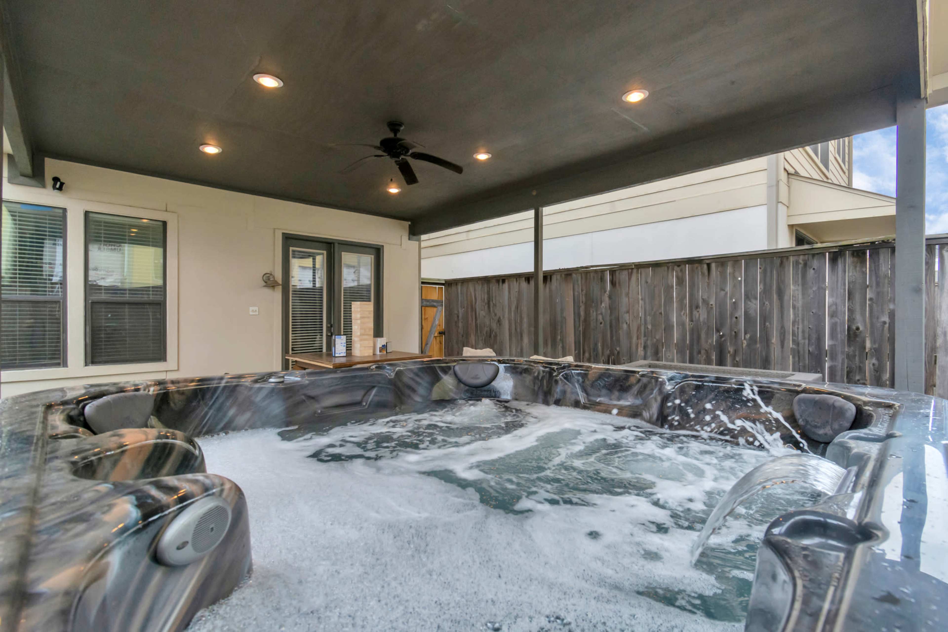 The image shows a hot tub with bubbles under a covered patio, adjacent to a wooden fence and a sliding glass door.