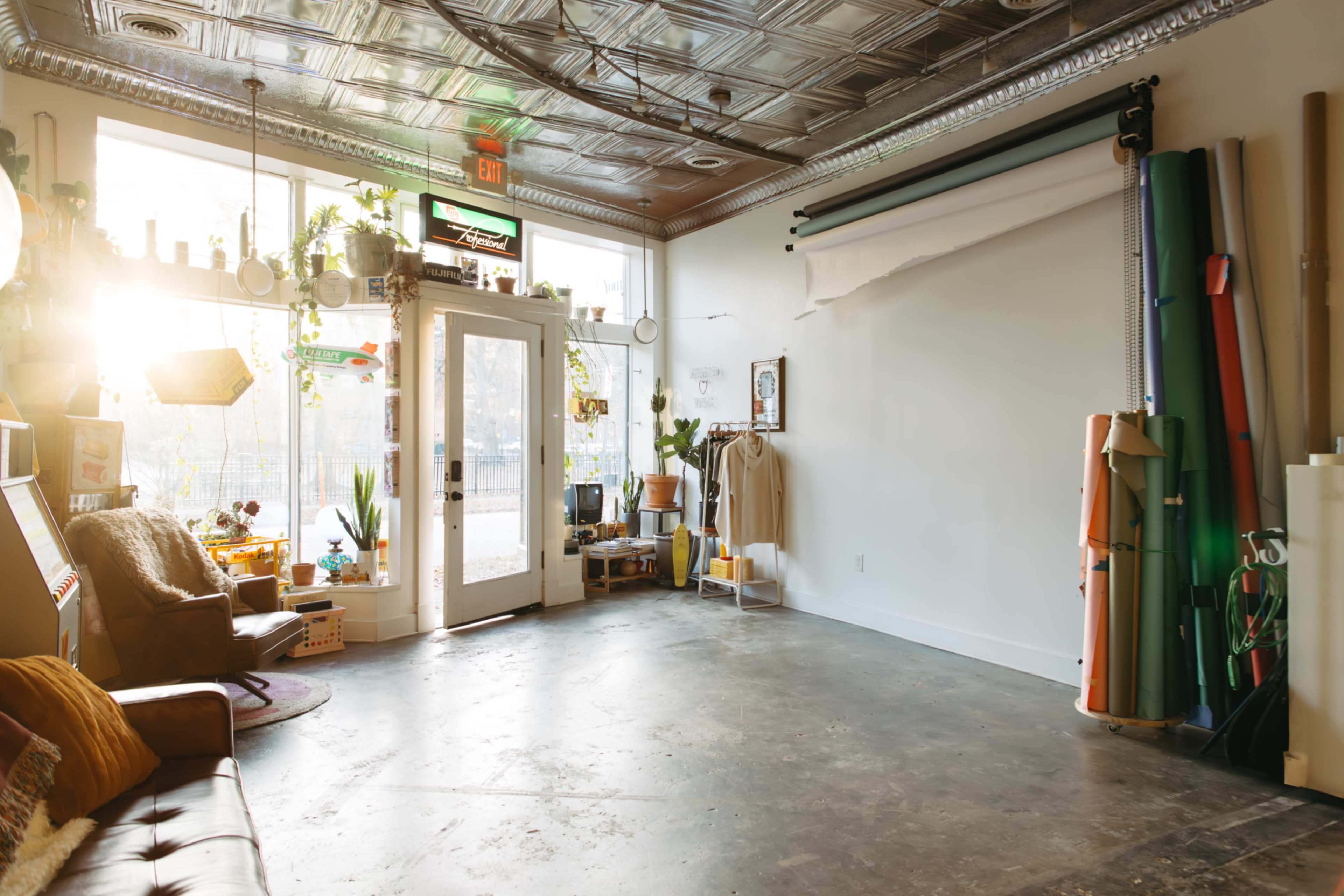 A bright, spacious interior of a studio features large windows, a wooden door, and various photography backdrops along the walls.