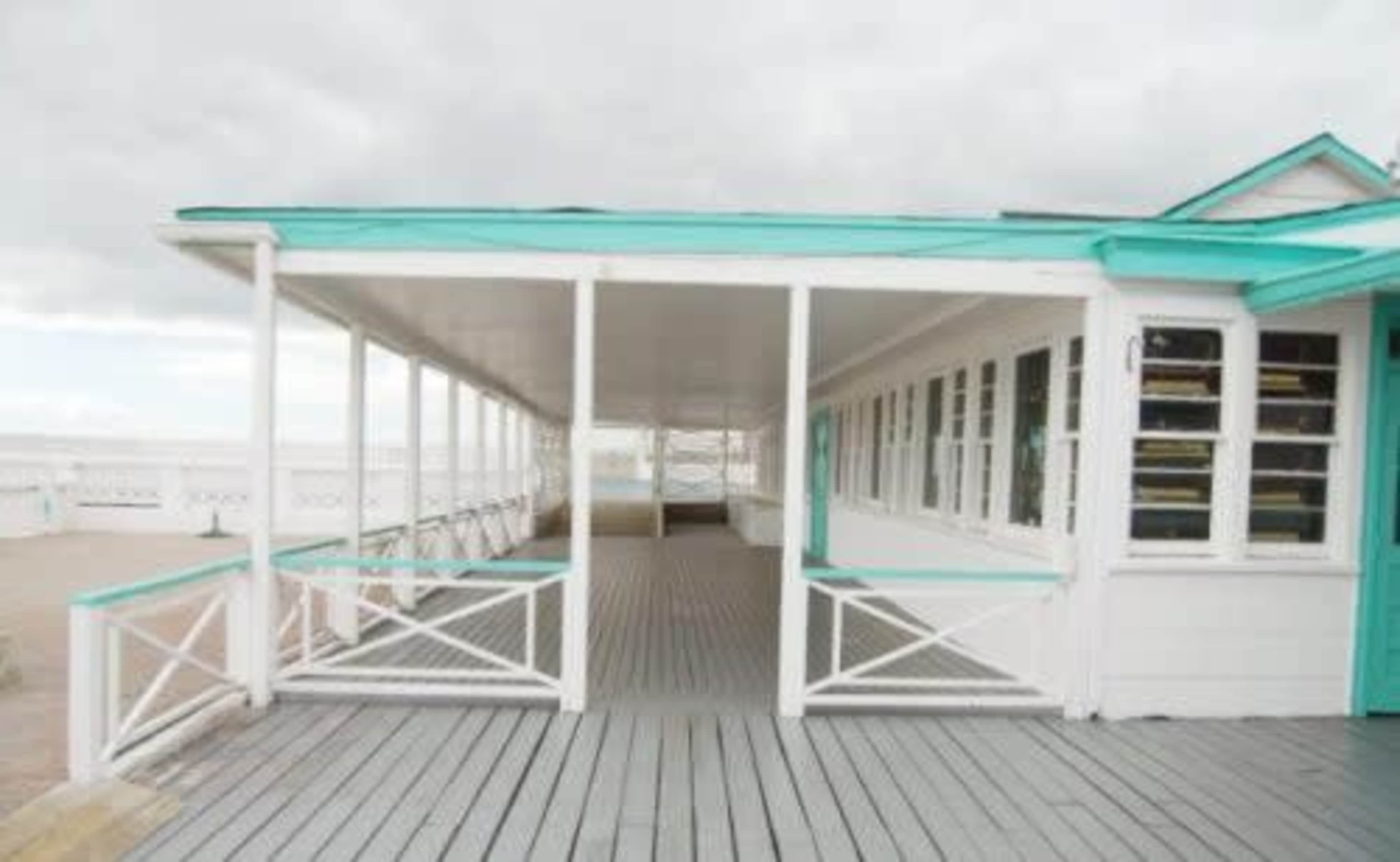 A seaside pavilion with a covered walkway and large windows overlooking the water.