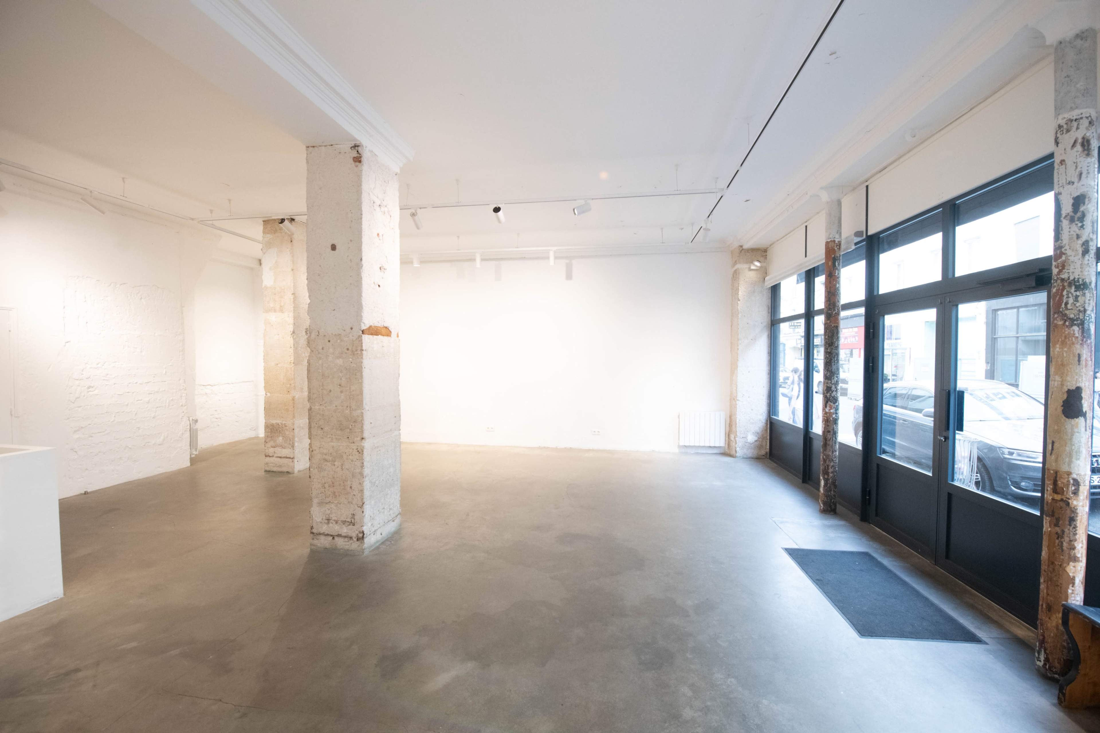 An empty gallery space with concrete floors, white walls, and large windows.