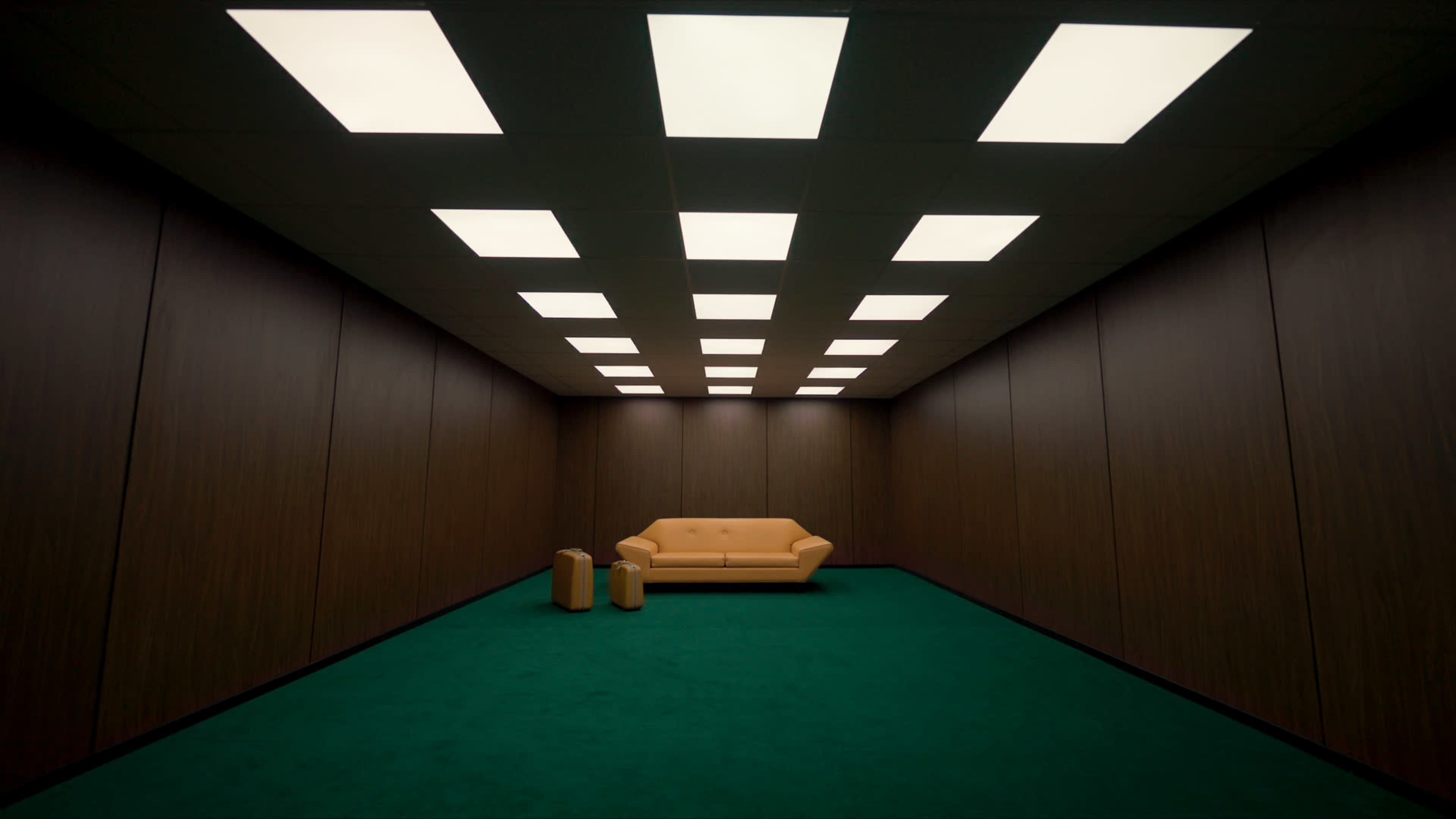 The image shows a minimalist room with green carpet, wooden paneling, a yellow couch, and two cylindrical objects.