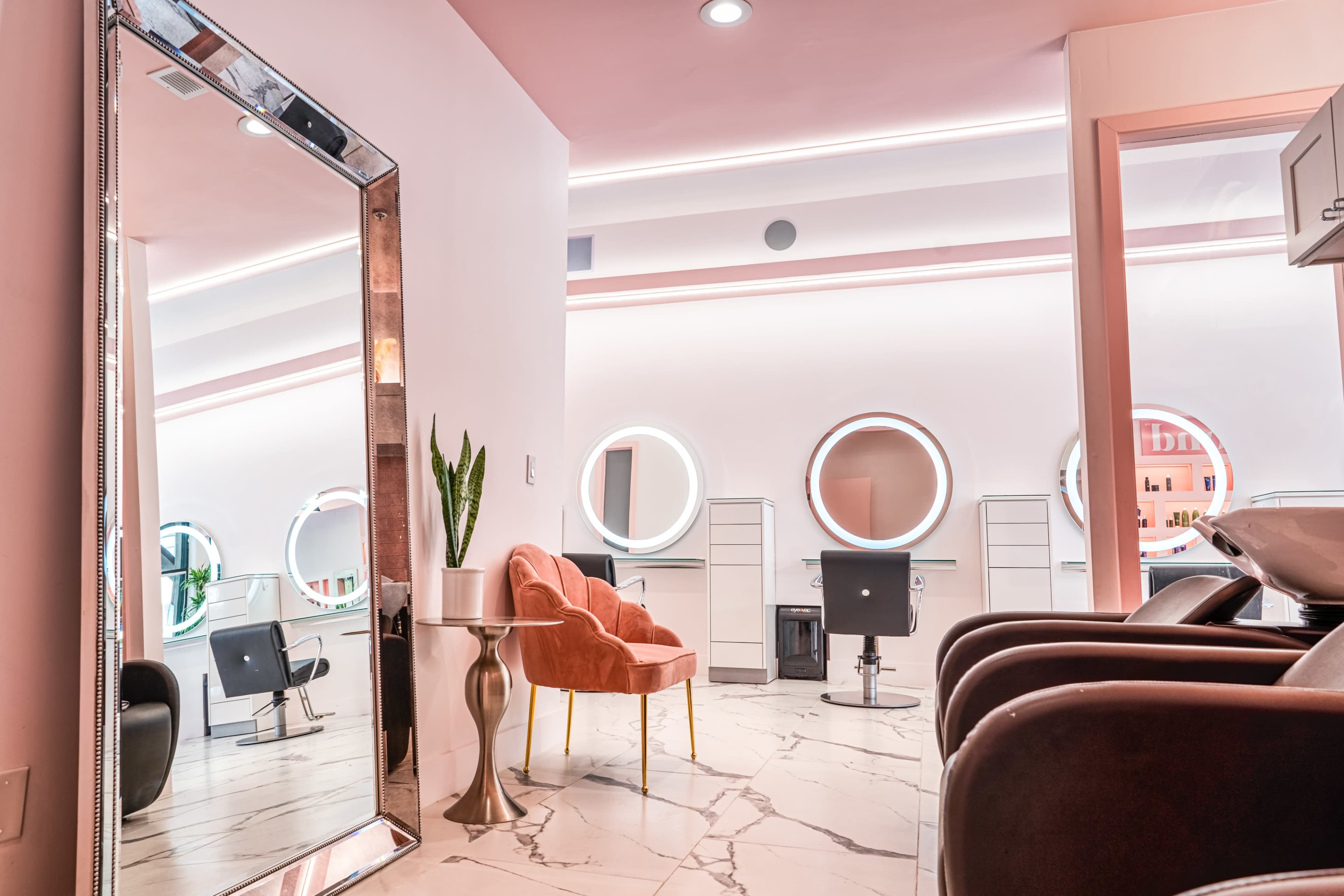A modern hair salon interior featuring a large mirror, circular mirrors on the walls, a stylish chair, and a marble floor.