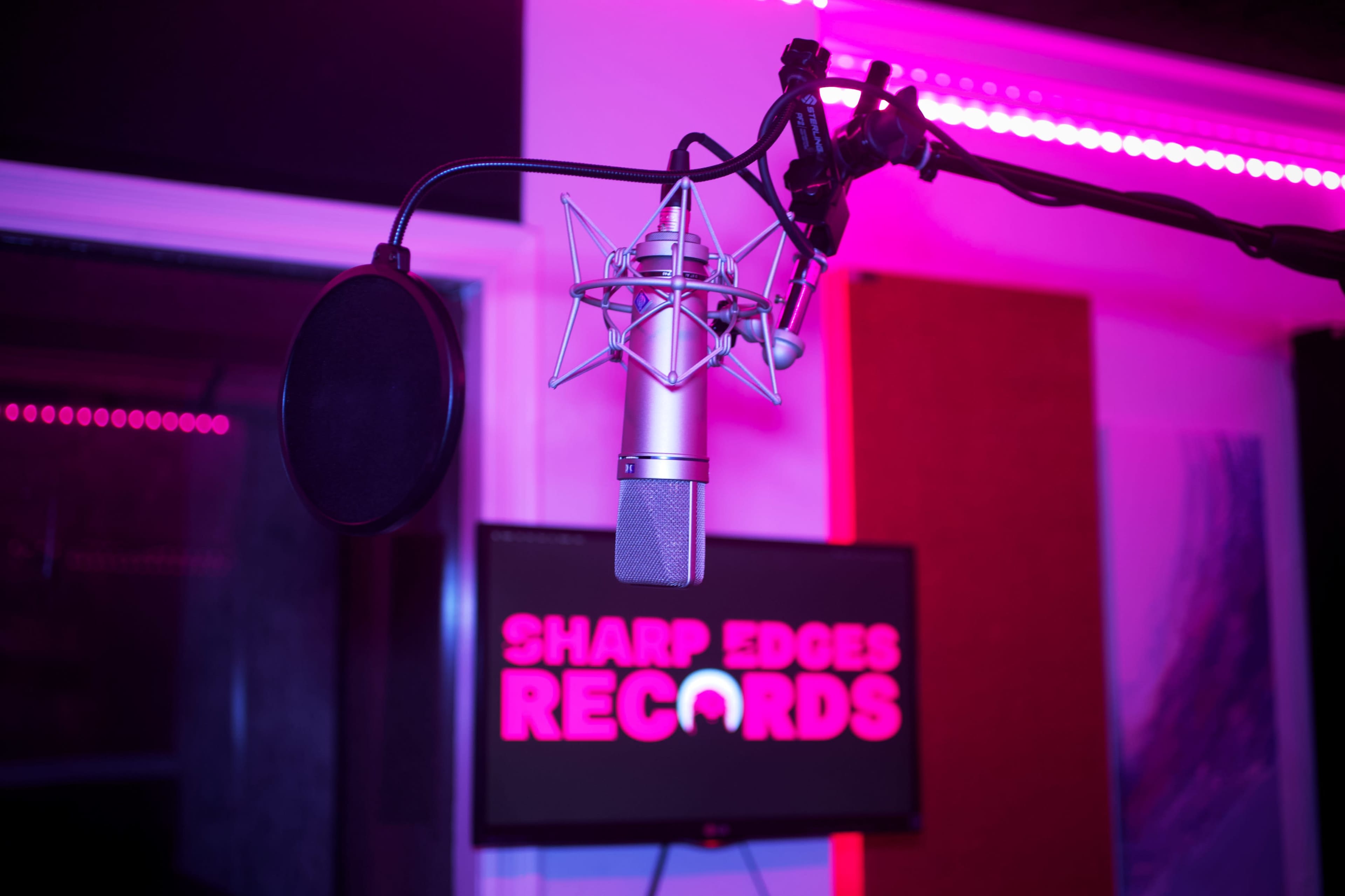 A microphone is positioned in front of a screen displaying the name "Sharp Edges Records" in bright pink letters.