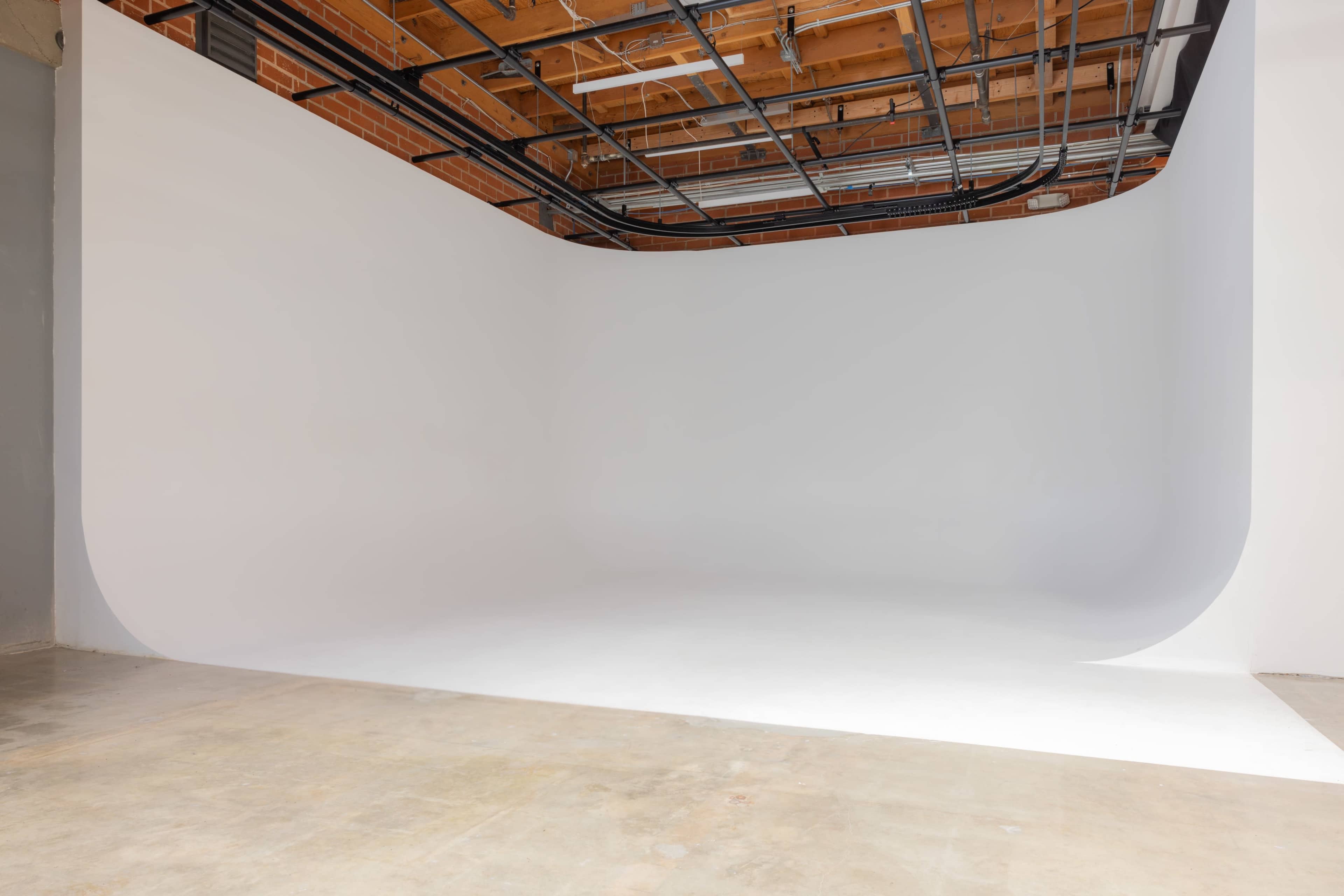 The image shows a spacious photography studio with a seamless white backdrop and exposed ceiling beams.