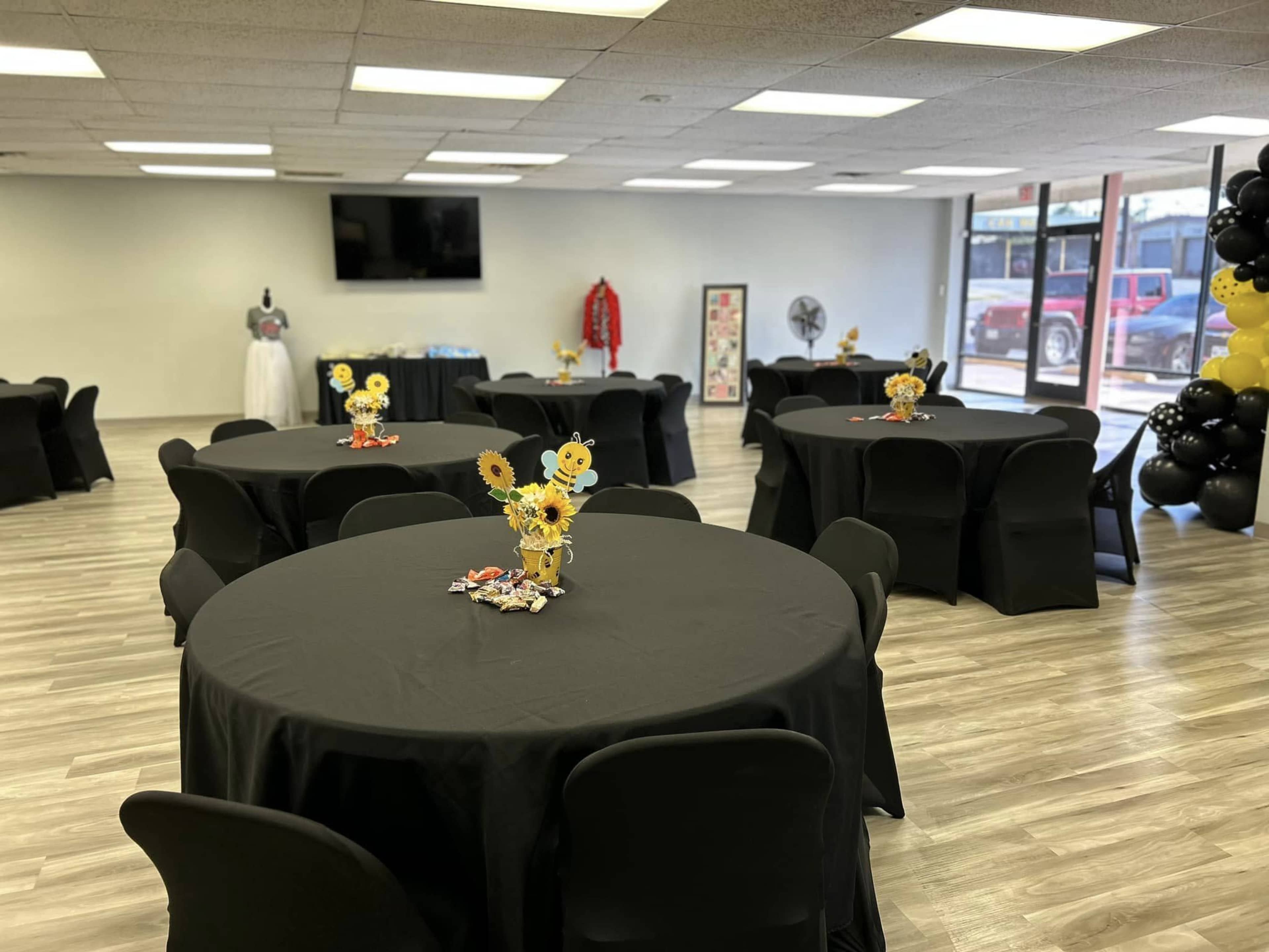 A spacious event room filled with several round tables covered in black tablecloths, each adorned with floral centerpieces.