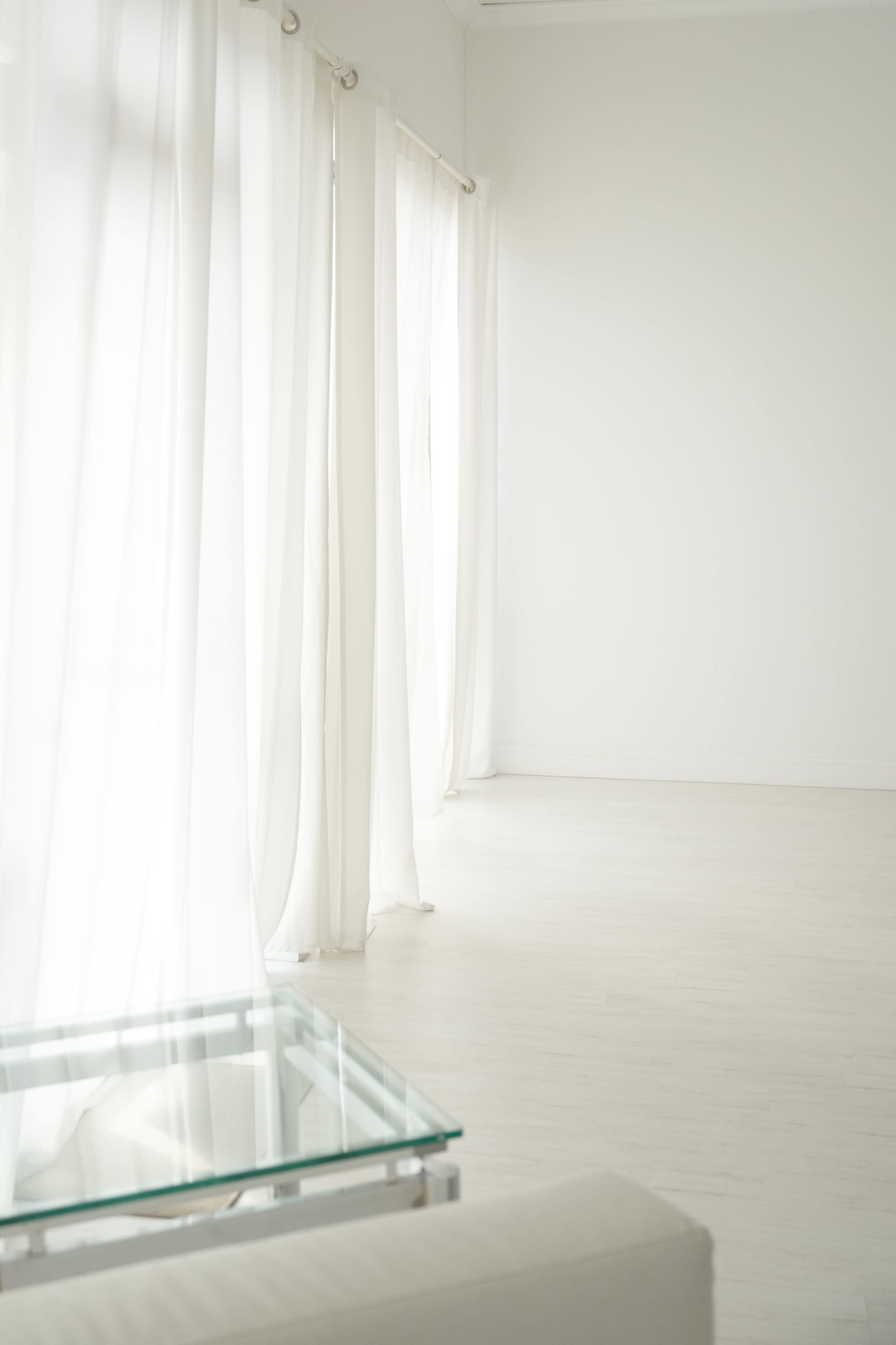 A sunlit interior features white sheer curtains and a glass-topped table against a minimalist backdrop.