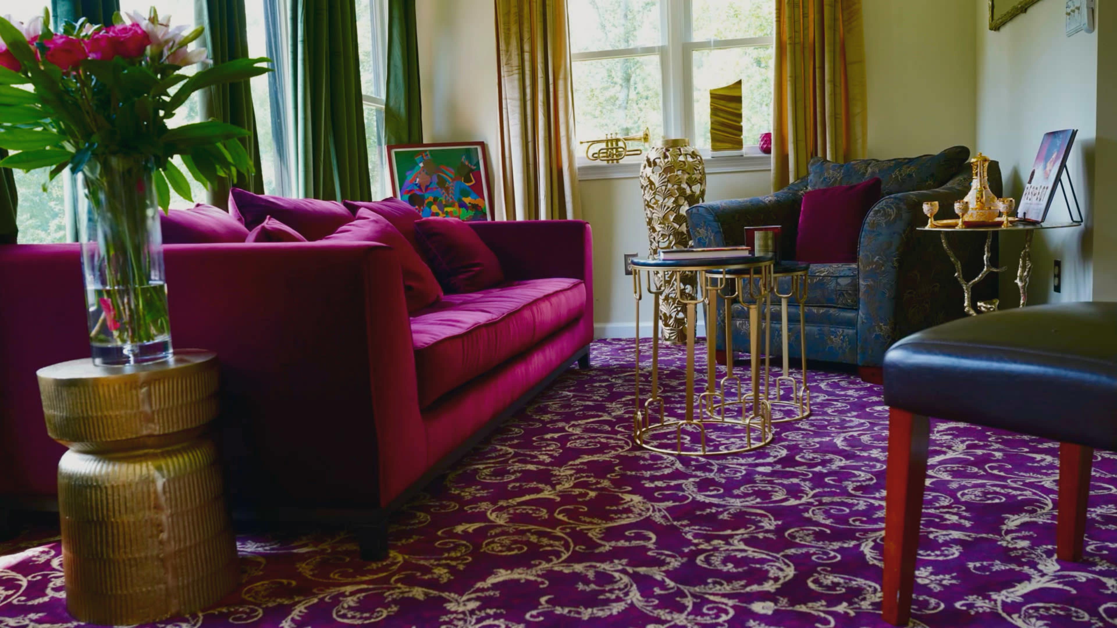 The scene features a room with a plush purple rug, a vibrant red sofa, a blue patterned armchair, and a decorative side table.