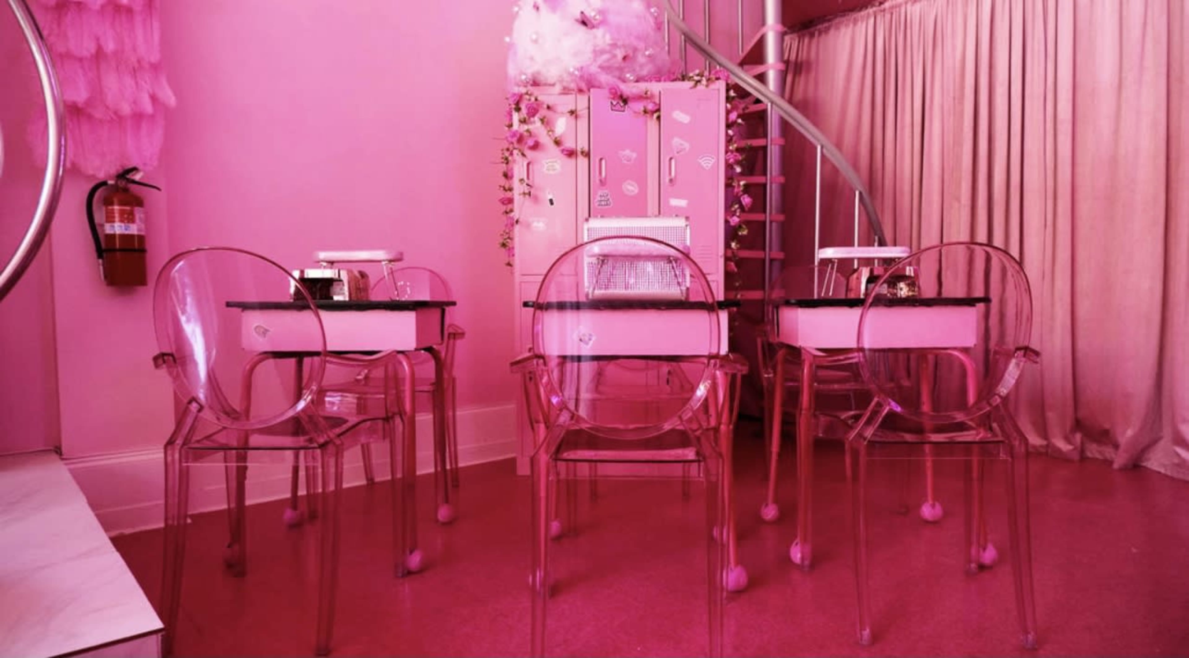 A pink-themed café interior with clear acrylic chairs arranged around black-topped tables.