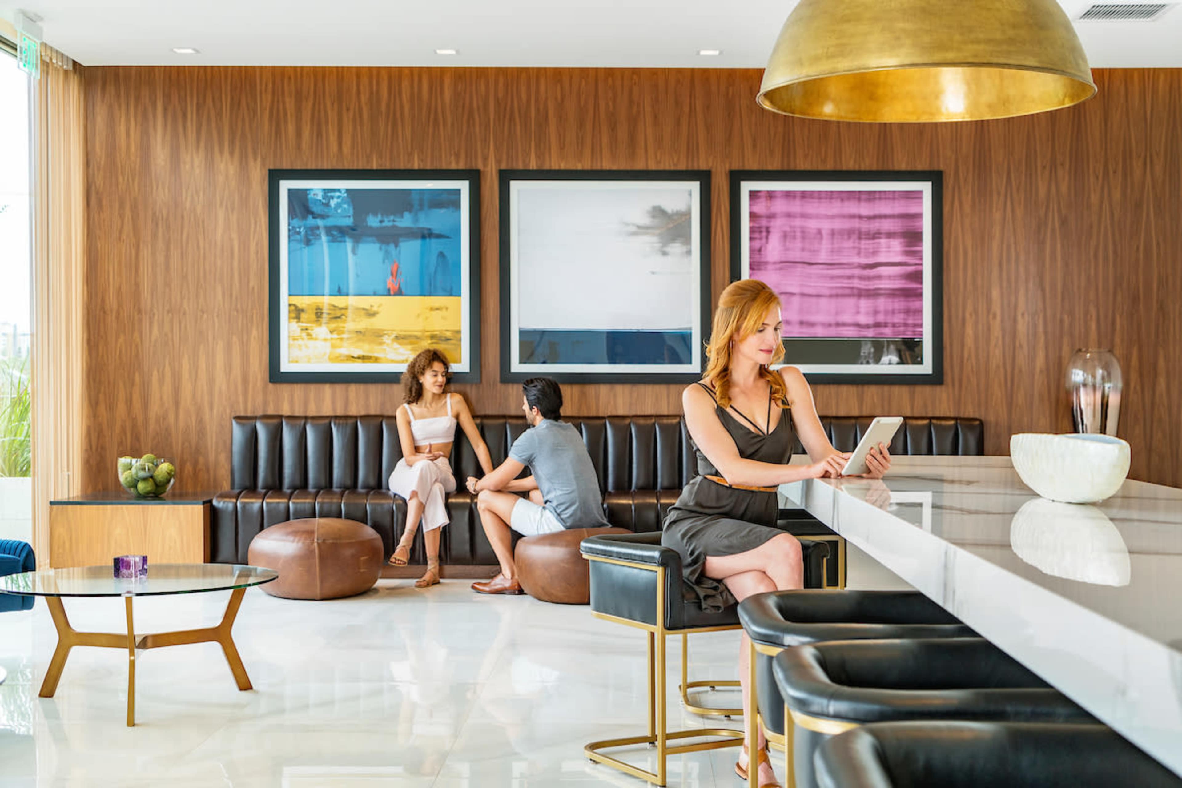 Three people relax in a modern lounge with large framed artworks on the wall and a sleek, white bar counter.