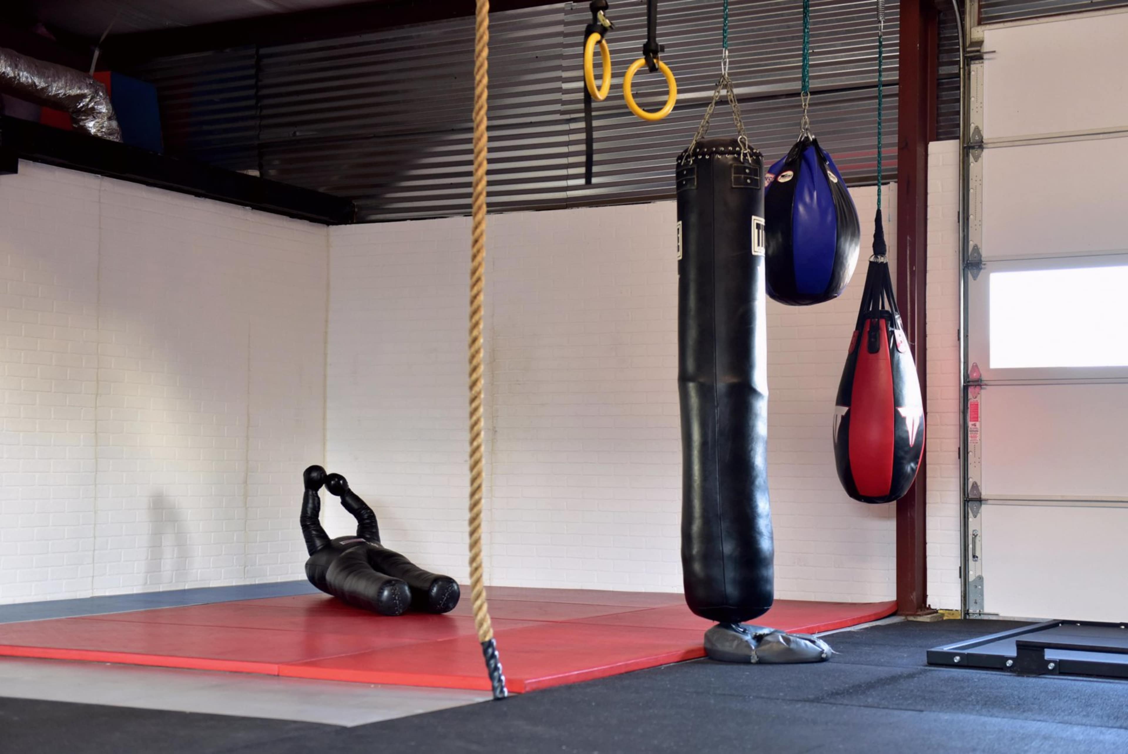 A gym interior with a red exercise mat, a punching bag, and a rope hanging from the ceiling.