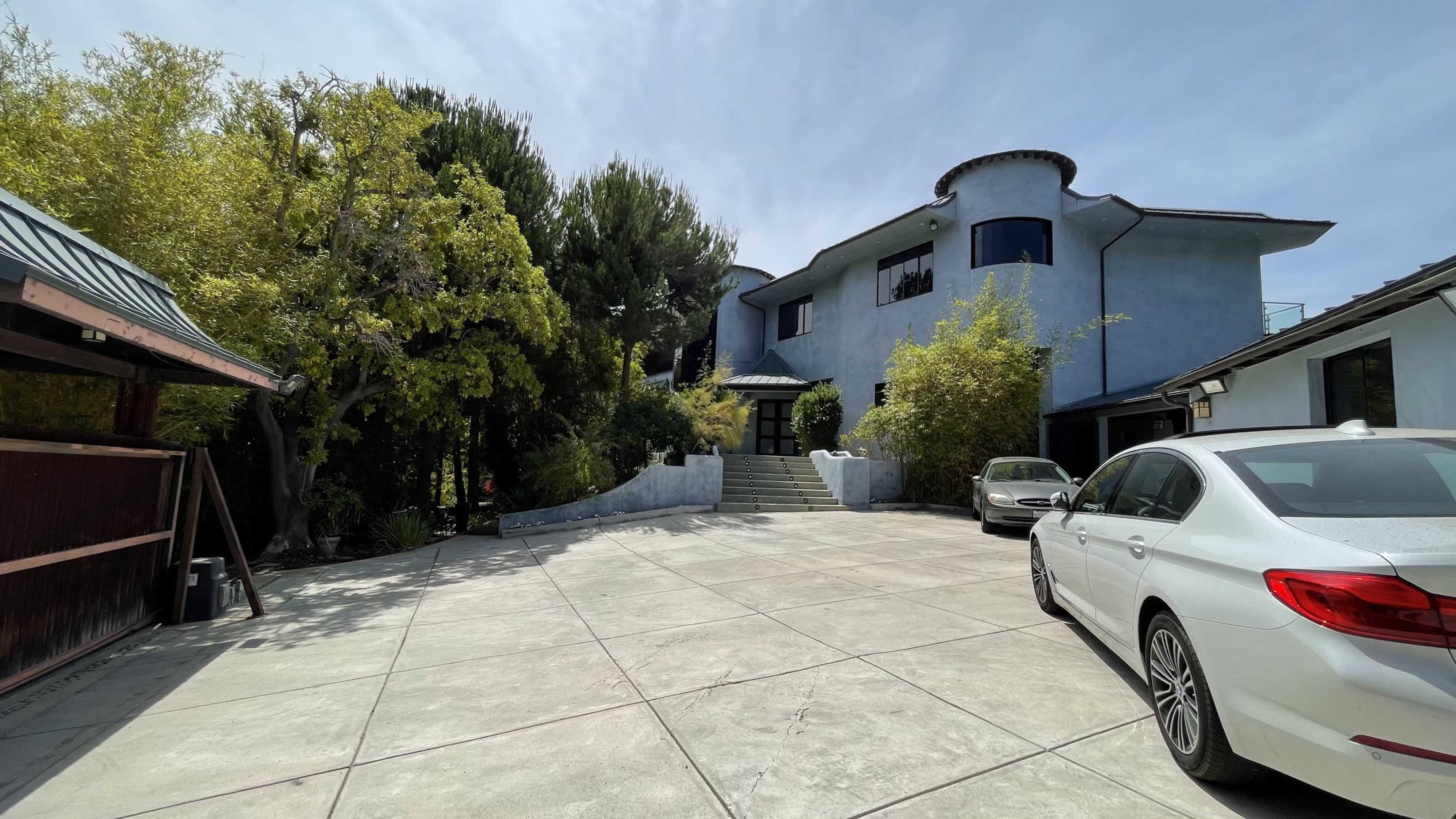 A modern multi-level house with a large driveway, surrounded by greenery and trees.