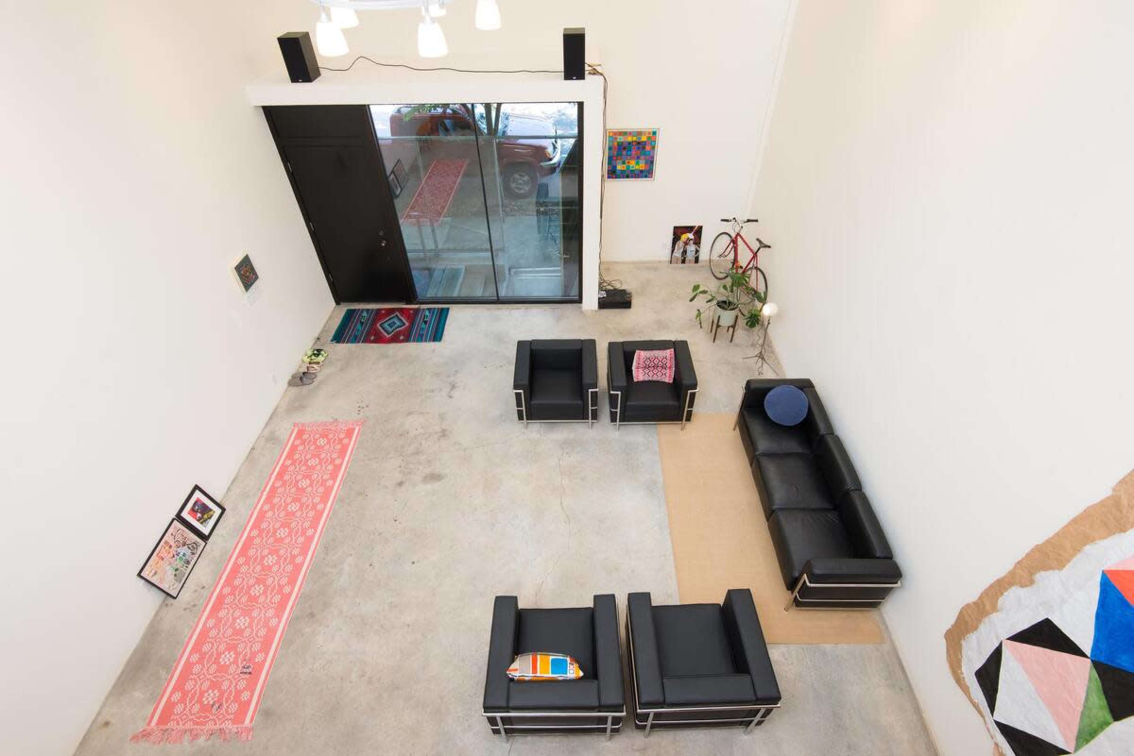 A minimalist interior space with four black chairs arranged around a small table, a colorful rug on the floor, and a large glass door leading outside.