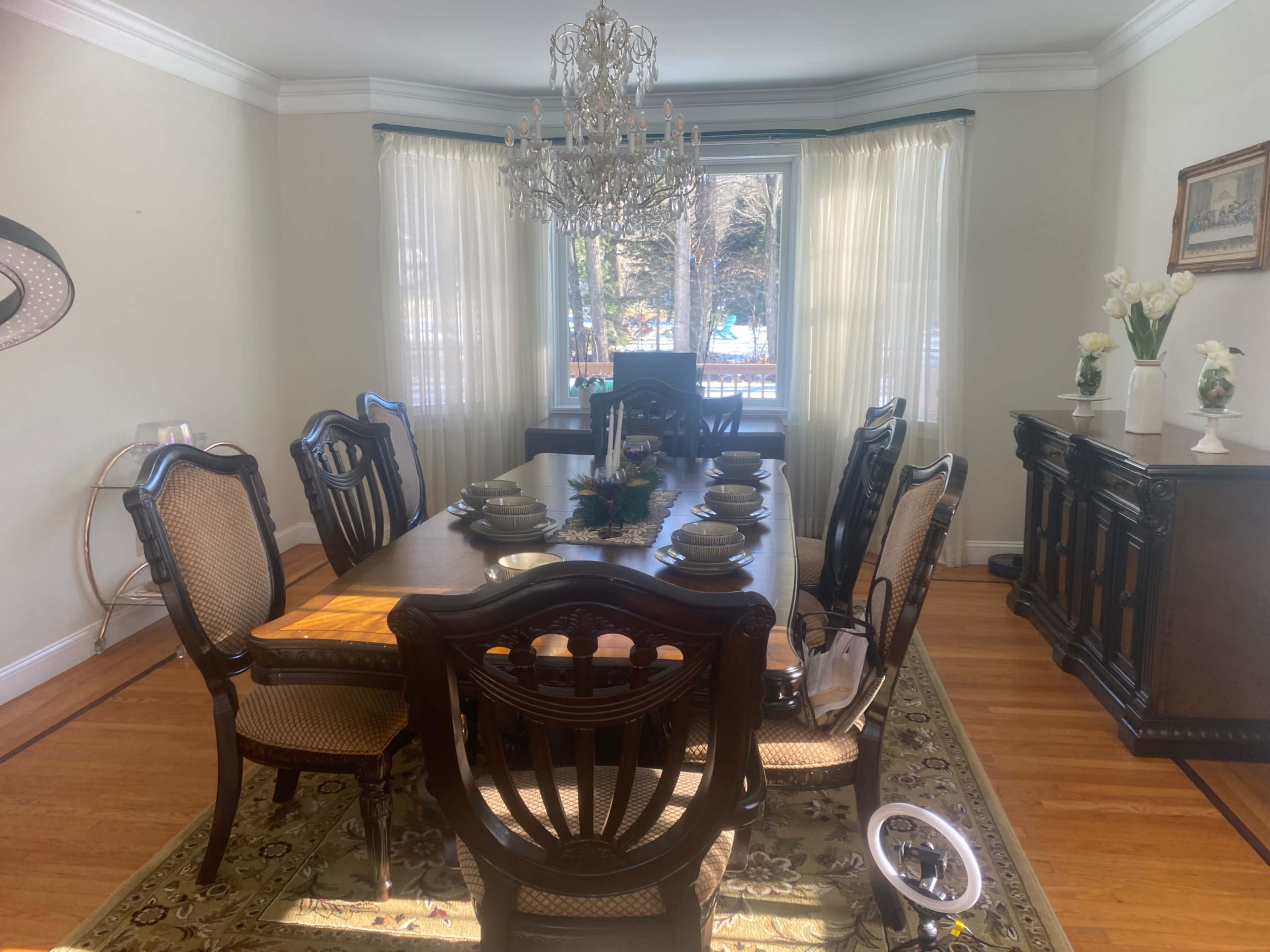 The dining room features a large wooden table set for six, with a chandelier overhead and large windows allowing natural light to fill the space.