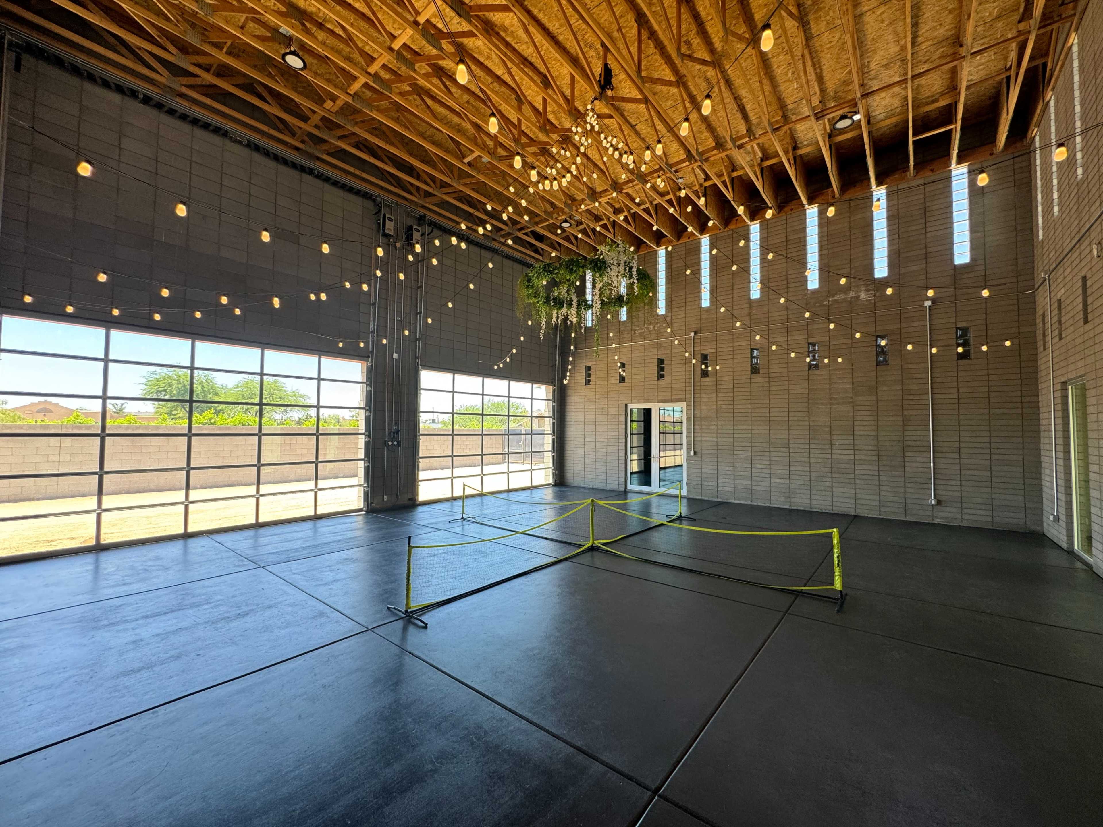 The interior of a spacious event hall features high ceilings, large windows, and decorative string lights, with a small area cordoned off by yellow tape.