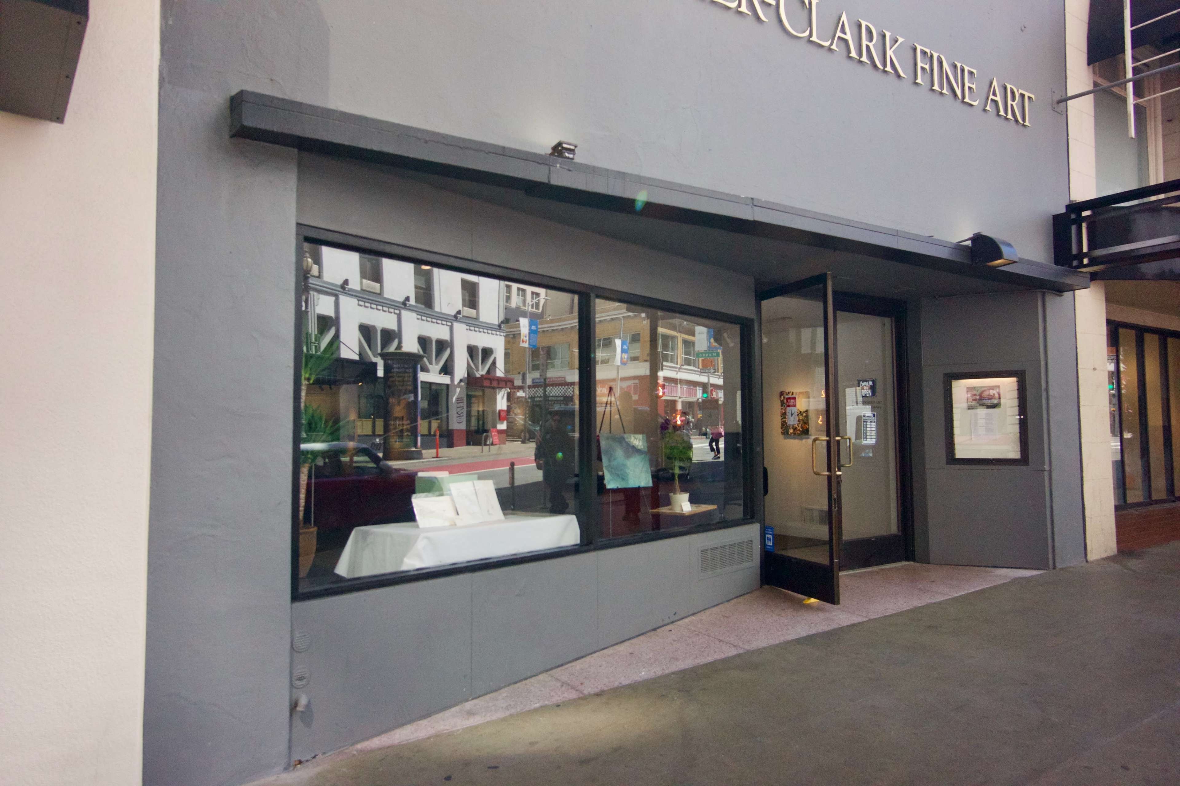 The exterior of a fine art gallery displays large windows and a main entrance, revealing a glimpse of the interior setup.