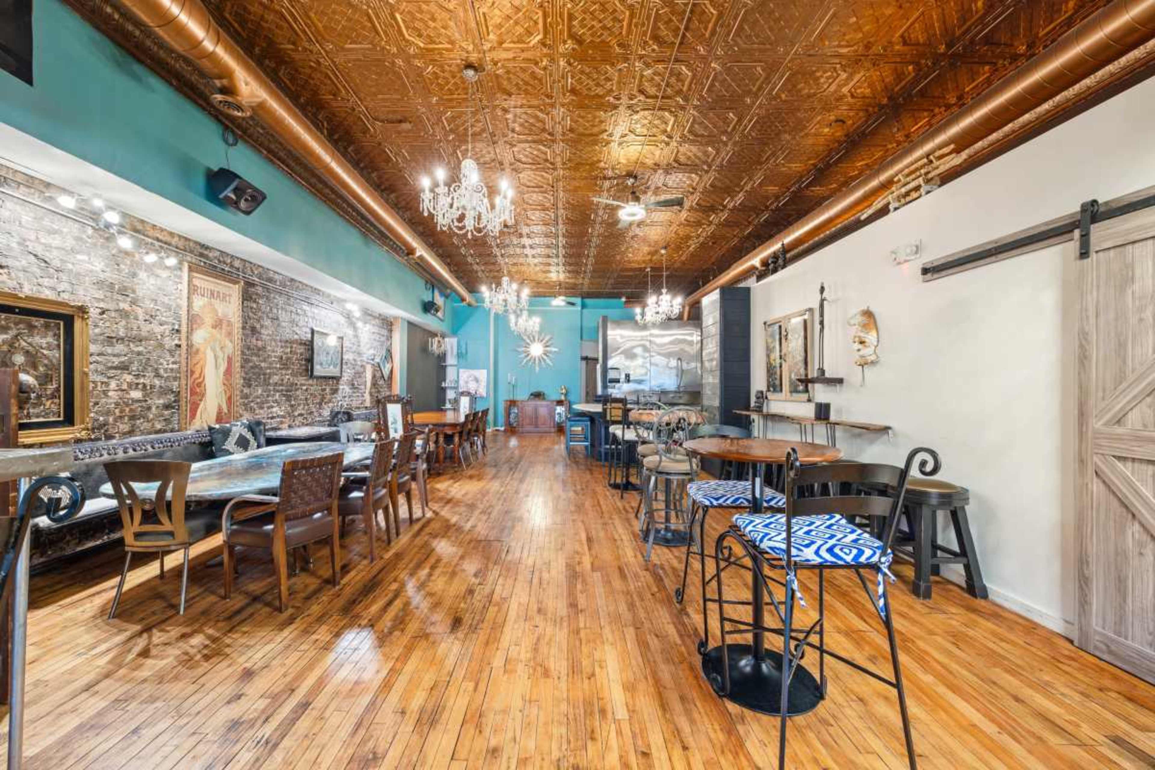 The image shows a restaurant interior with wooden flooring, exposed brick walls, decorative chandeliers, and a mix of seating arrangements along the length of the space.