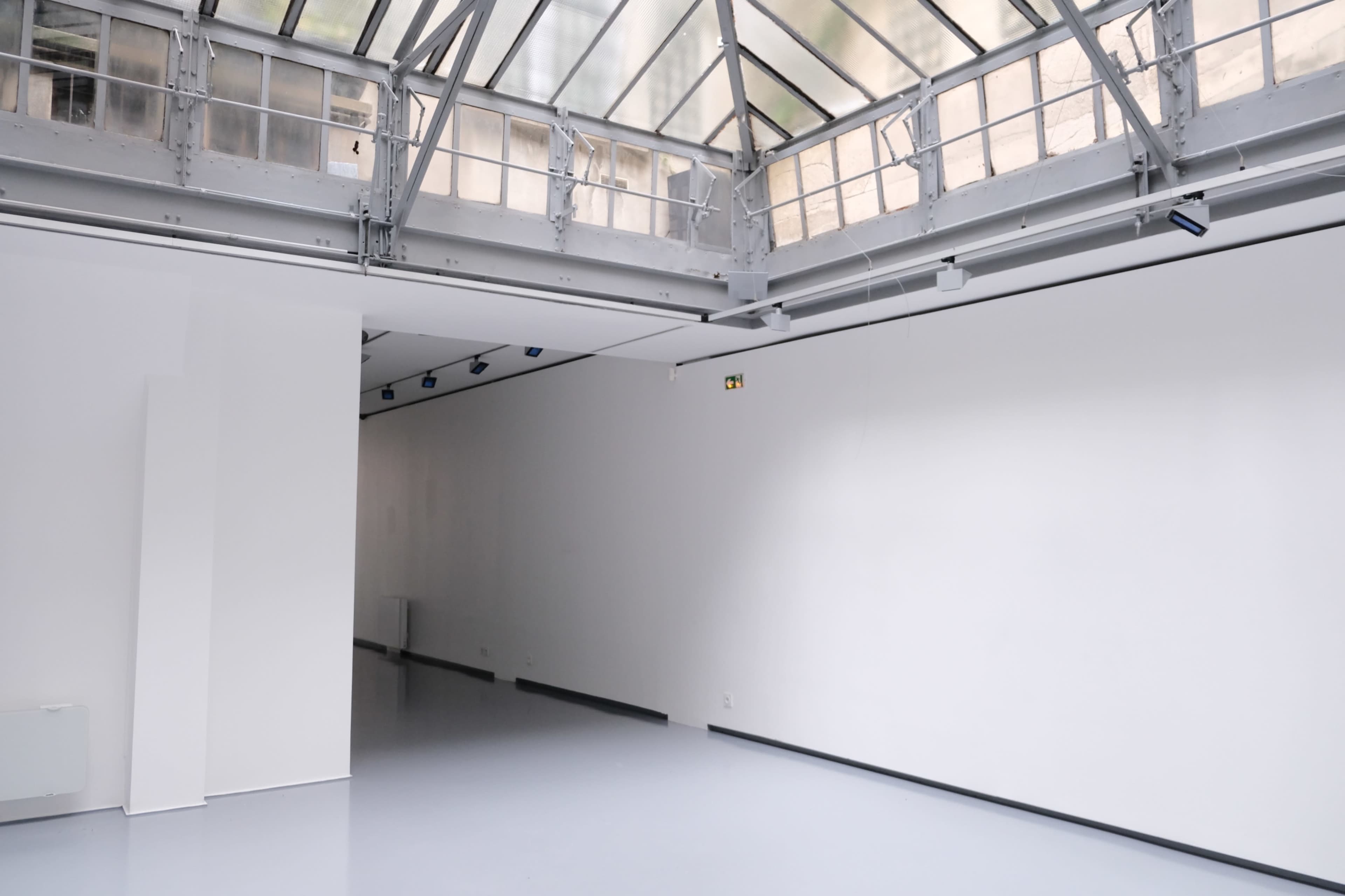 The image shows a bright, minimalistic gallery space with white walls and a glass roof.