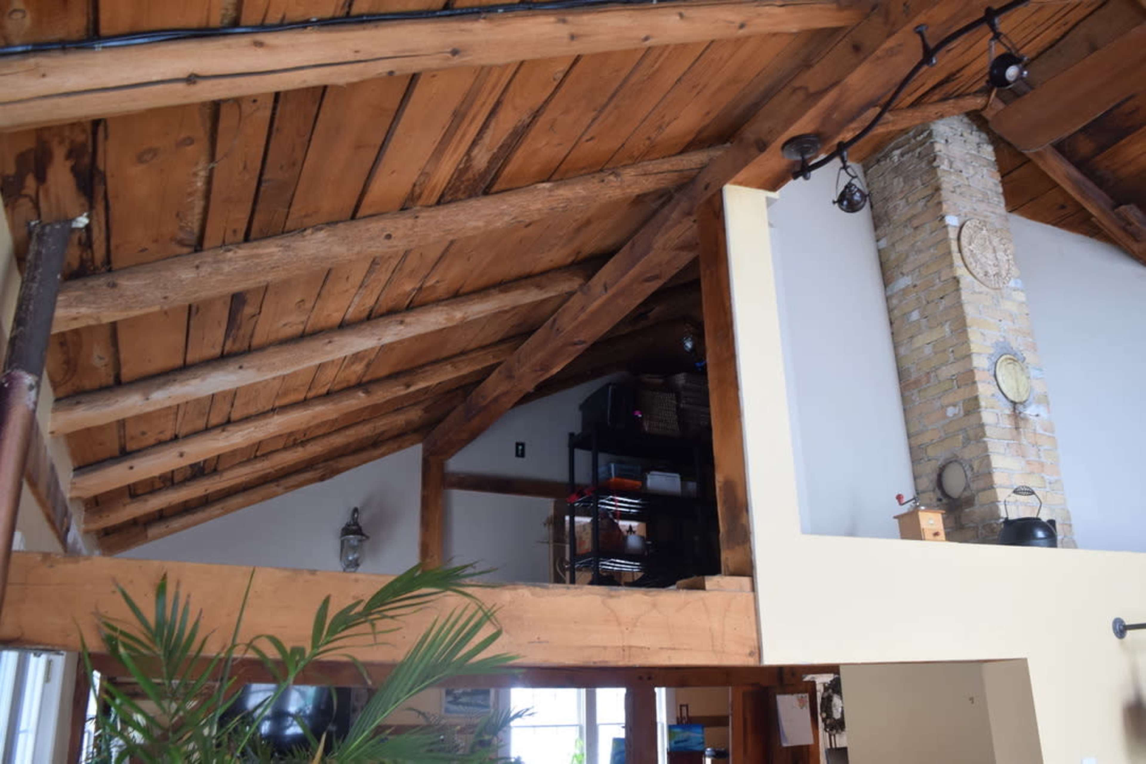 A vaulted wooden ceiling with exposed beams and a stone chimney, leading to a loft area in a residential space.