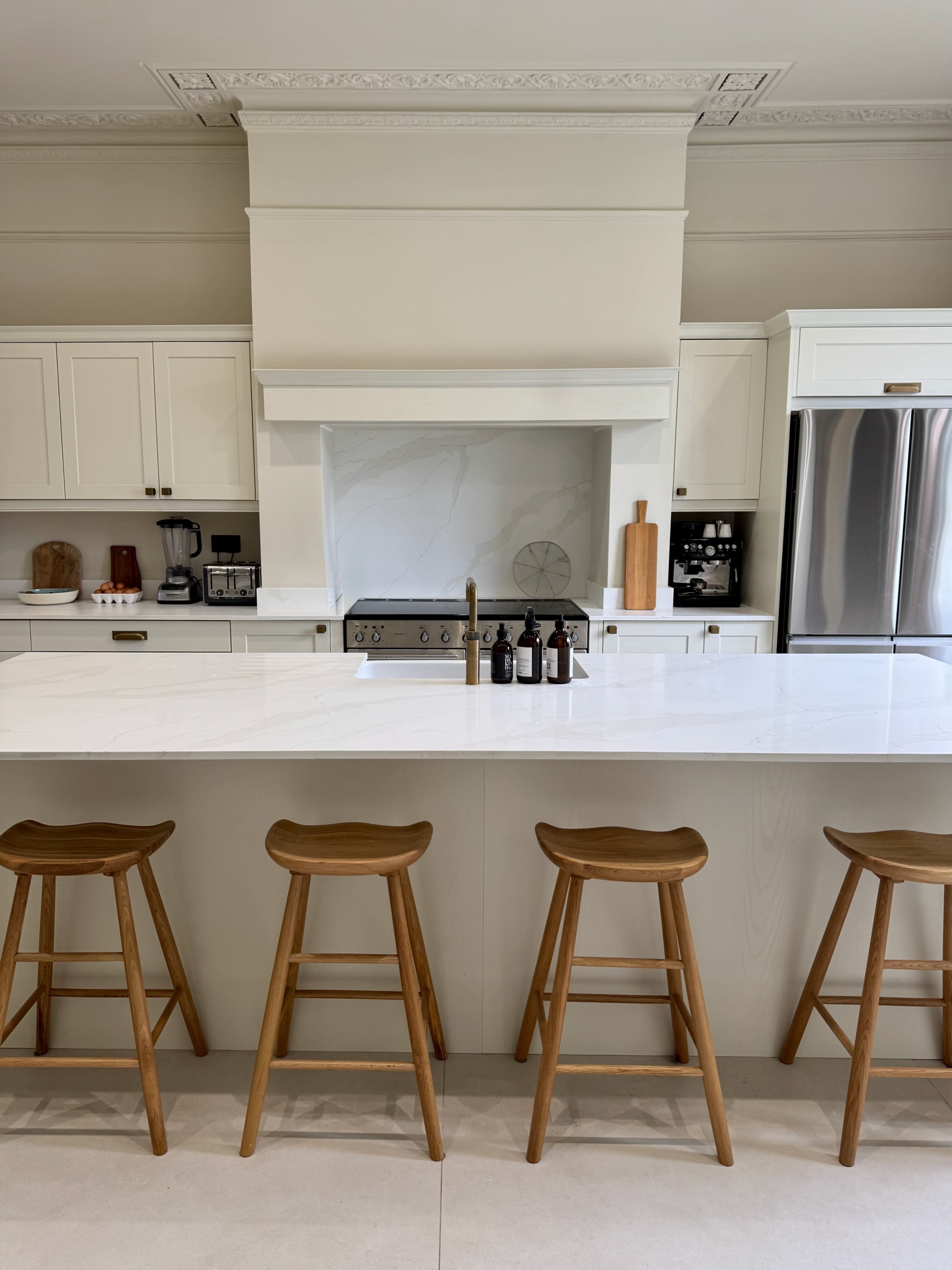 A modern kitchen features a large white island with wooden bar stools, sleek cabinetry, and stainless steel appliances.