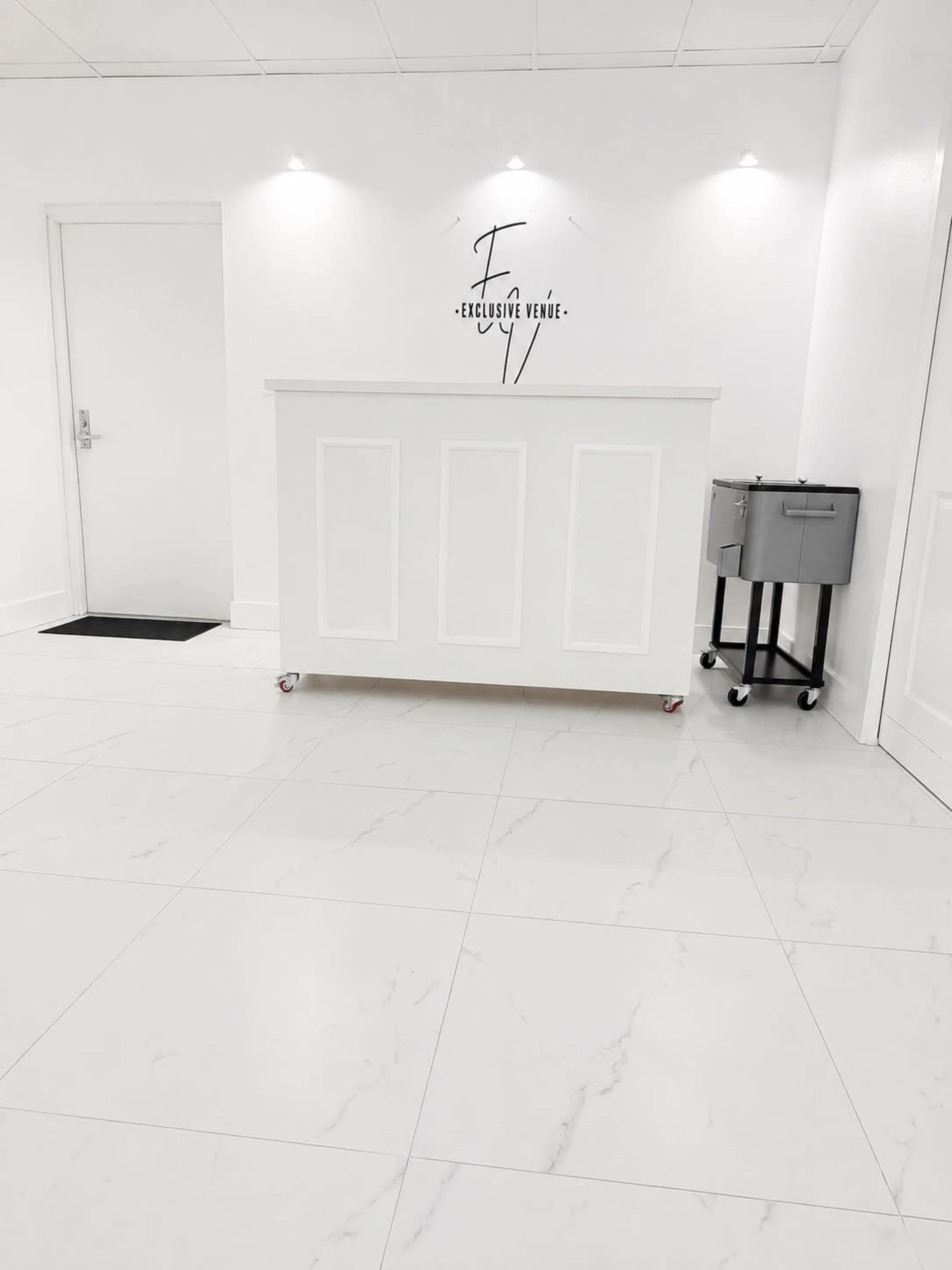 The image shows a modern reception area with a white counter, light-colored walls, and glossy tiled flooring.