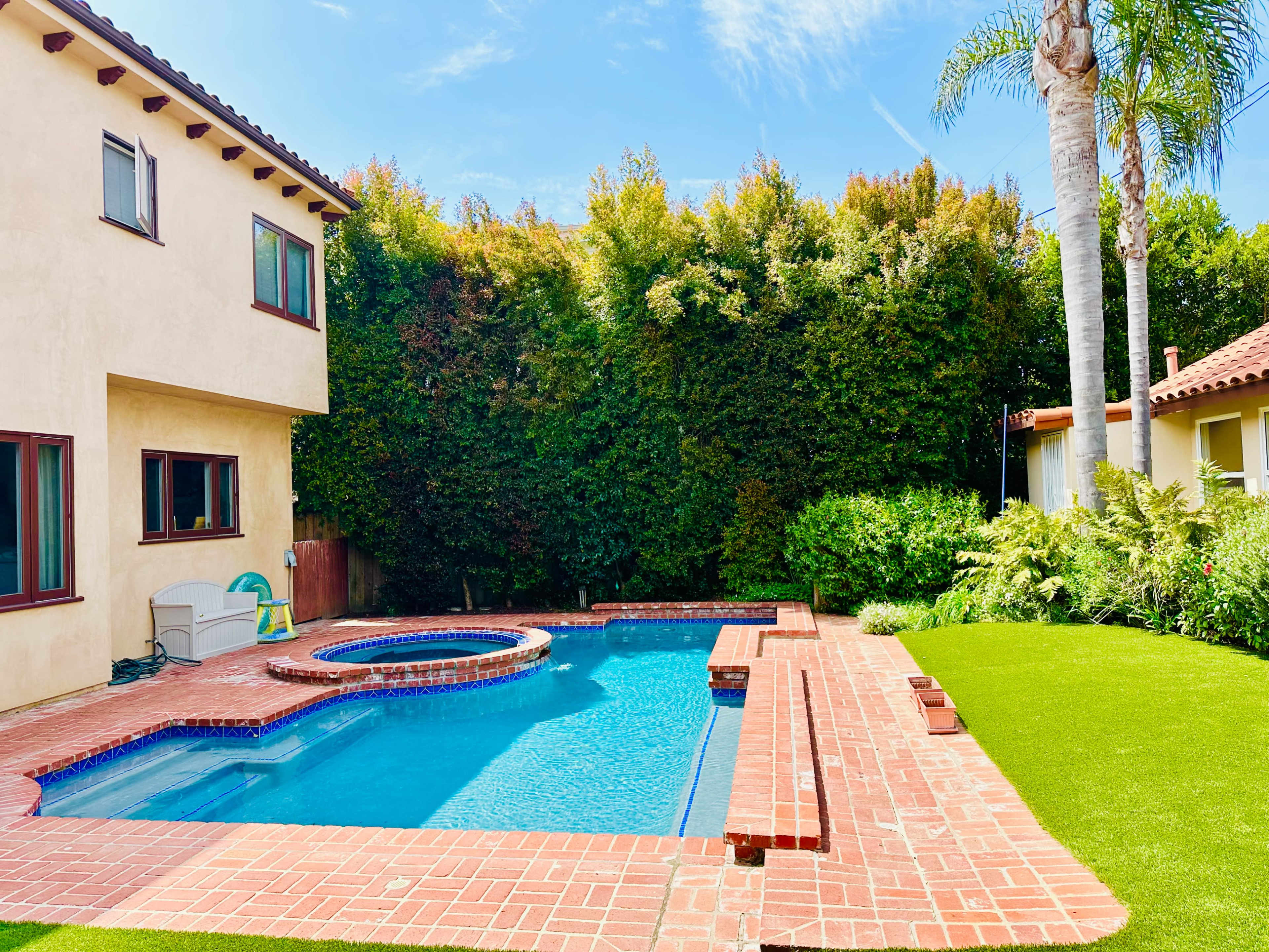 A swimming pool with a spa and patio area is surrounded by lush greenery and a well-maintained lawn.
