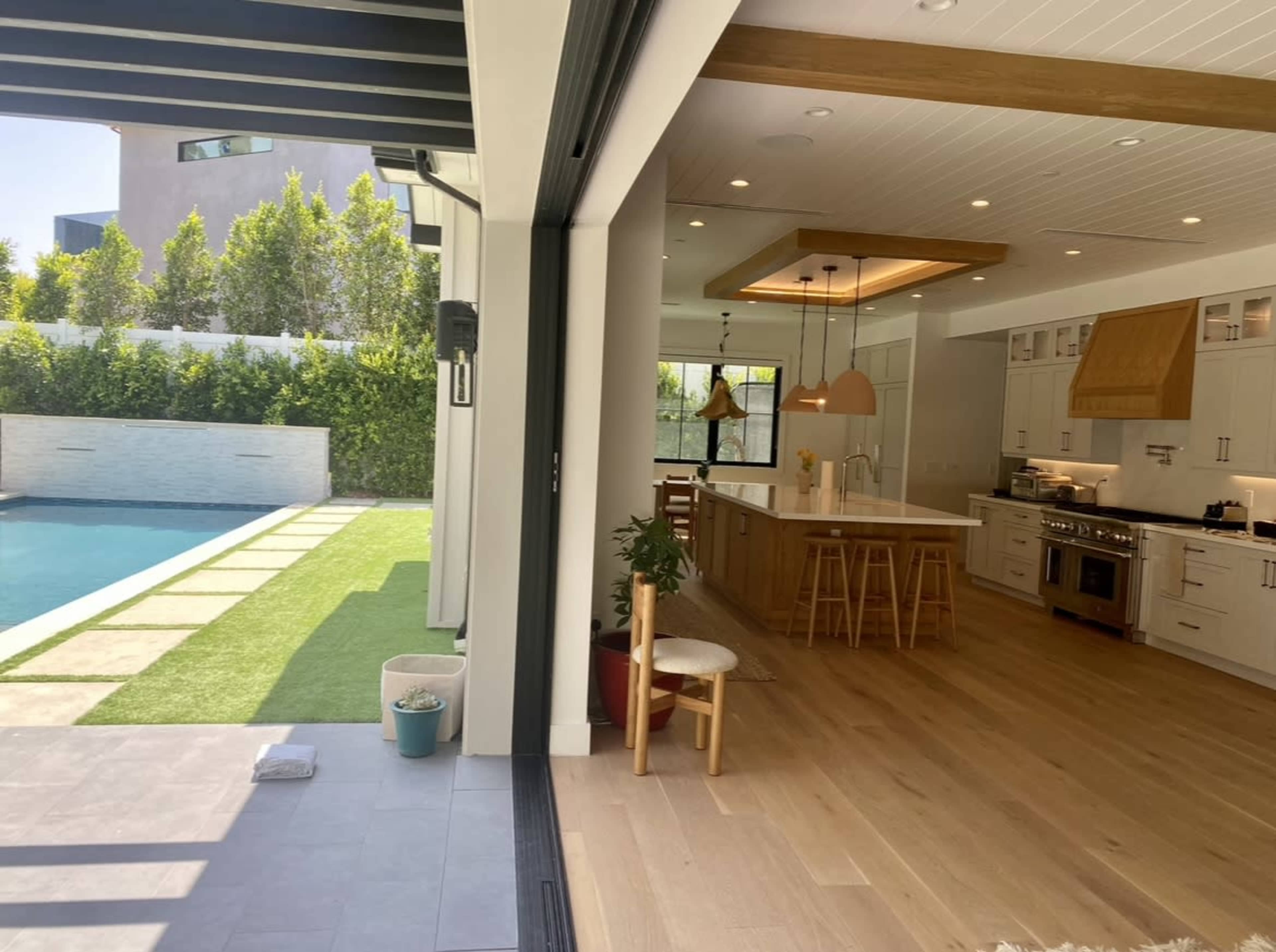 A modern kitchen opens up to a patio with a pool and well-maintained grass.