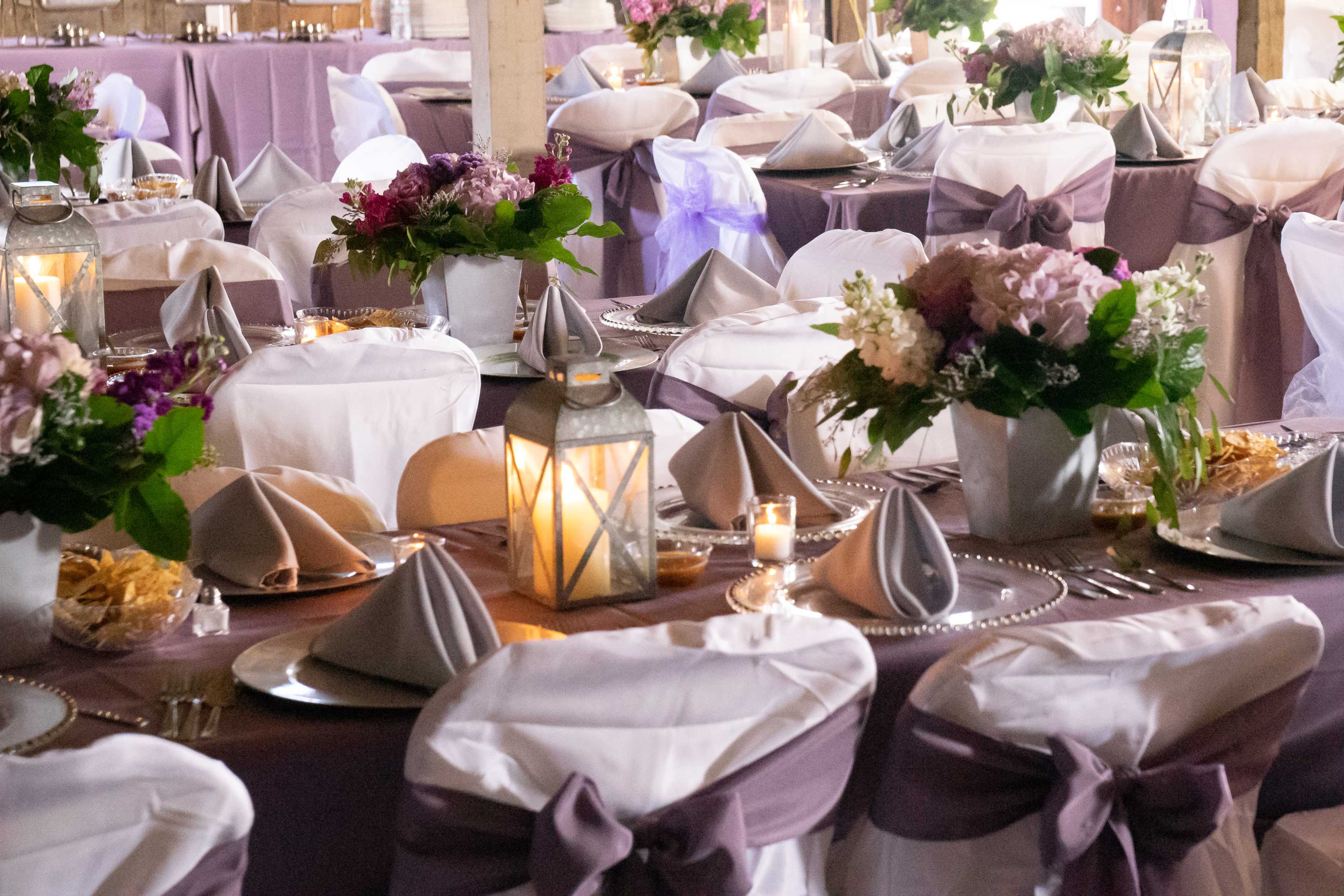 Elegantly set dining tables with floral centerpieces, neatly folded napkins, and soft lighting in a decorated venue.