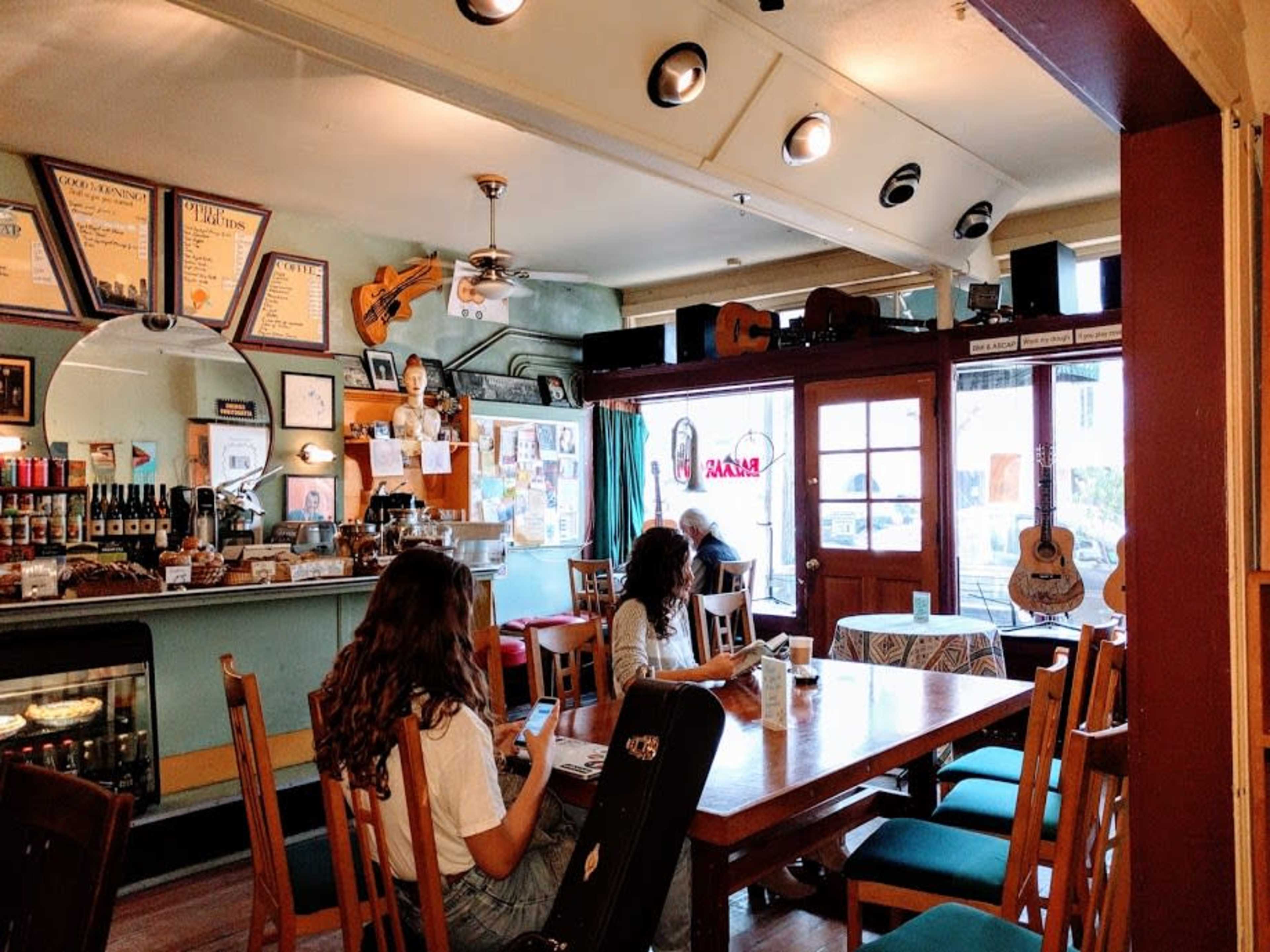 A cozy cafe features a wooden table surrounded by patrons, with walls adorned with musical instruments and framed photographs.
