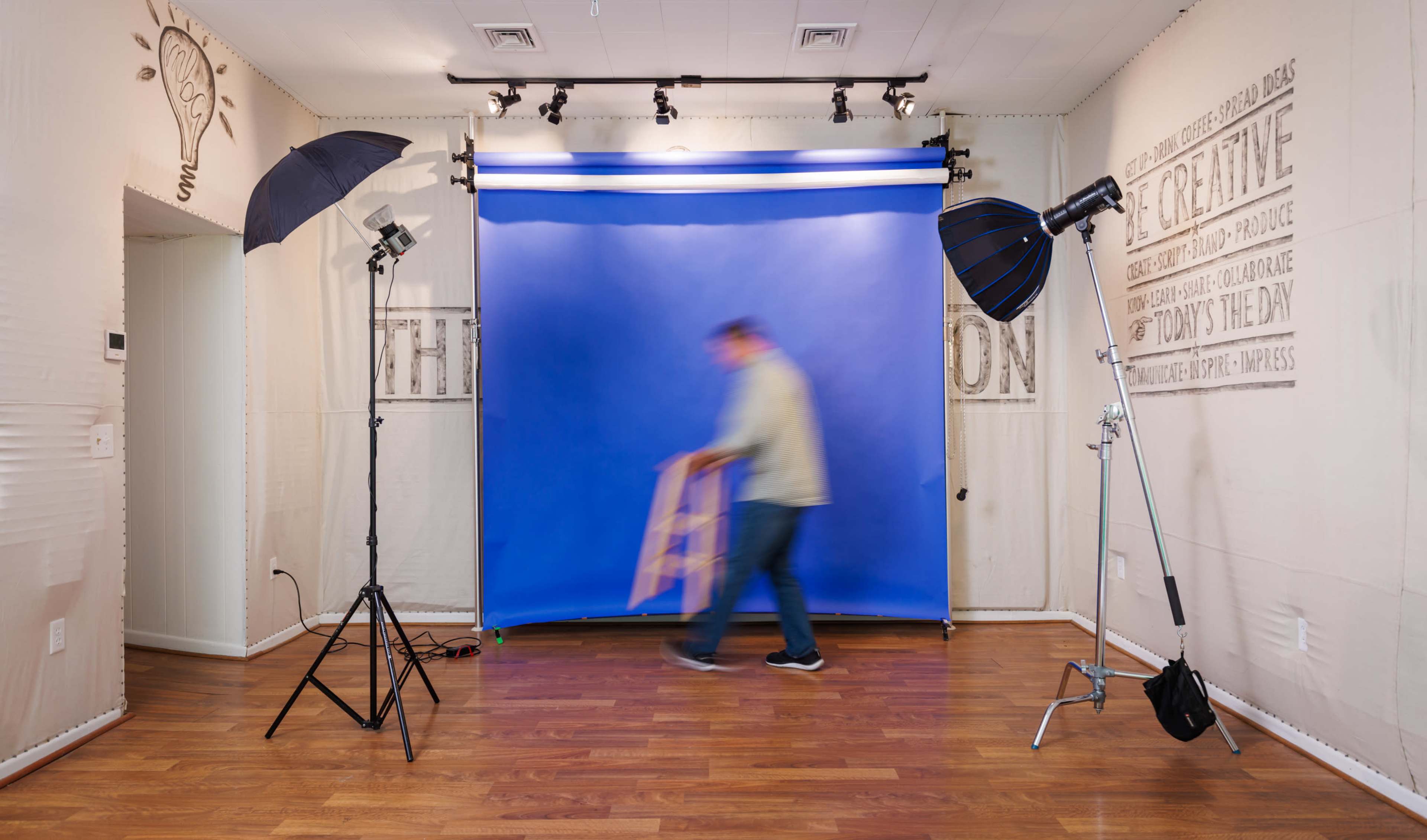 A person is moving a stool in a photography studio with a blue backdrop and lighting equipment set up.
