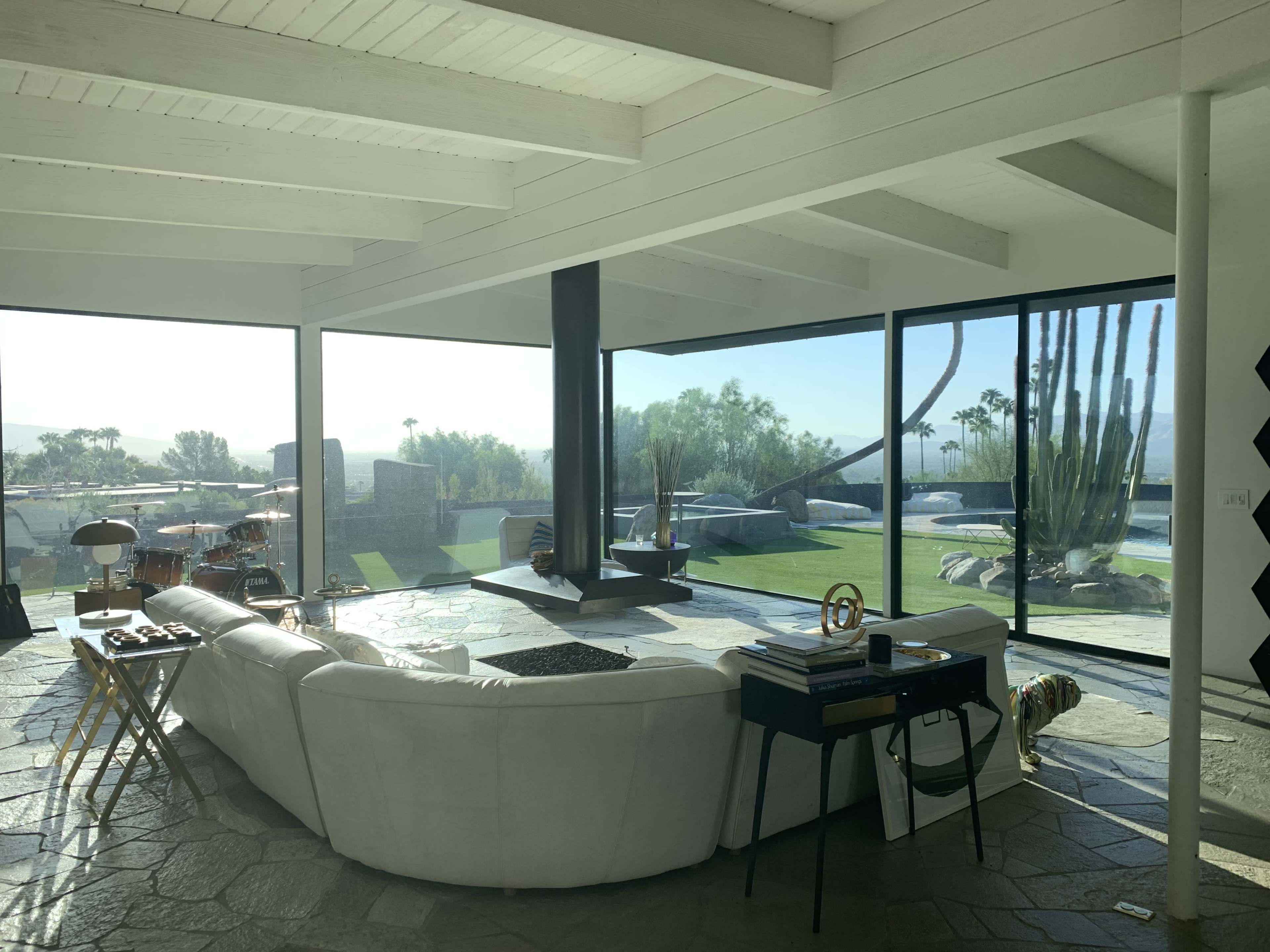 A spacious living room with large windows offering a view of a green landscape and palm trees.