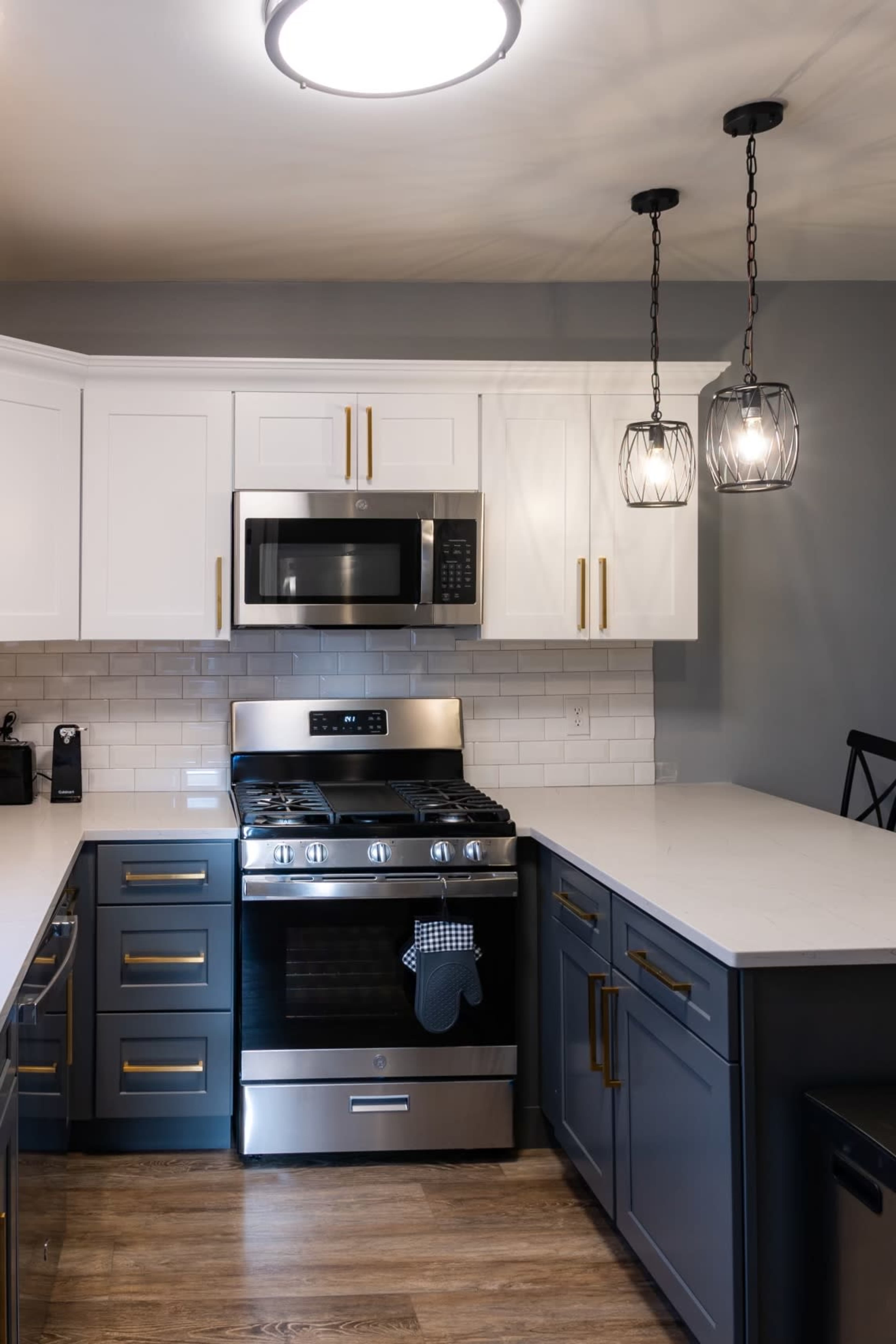 A modern kitchen with white and gray cabinetry, a stainless steel gas stove, microwave, and pendant lighting above an island.