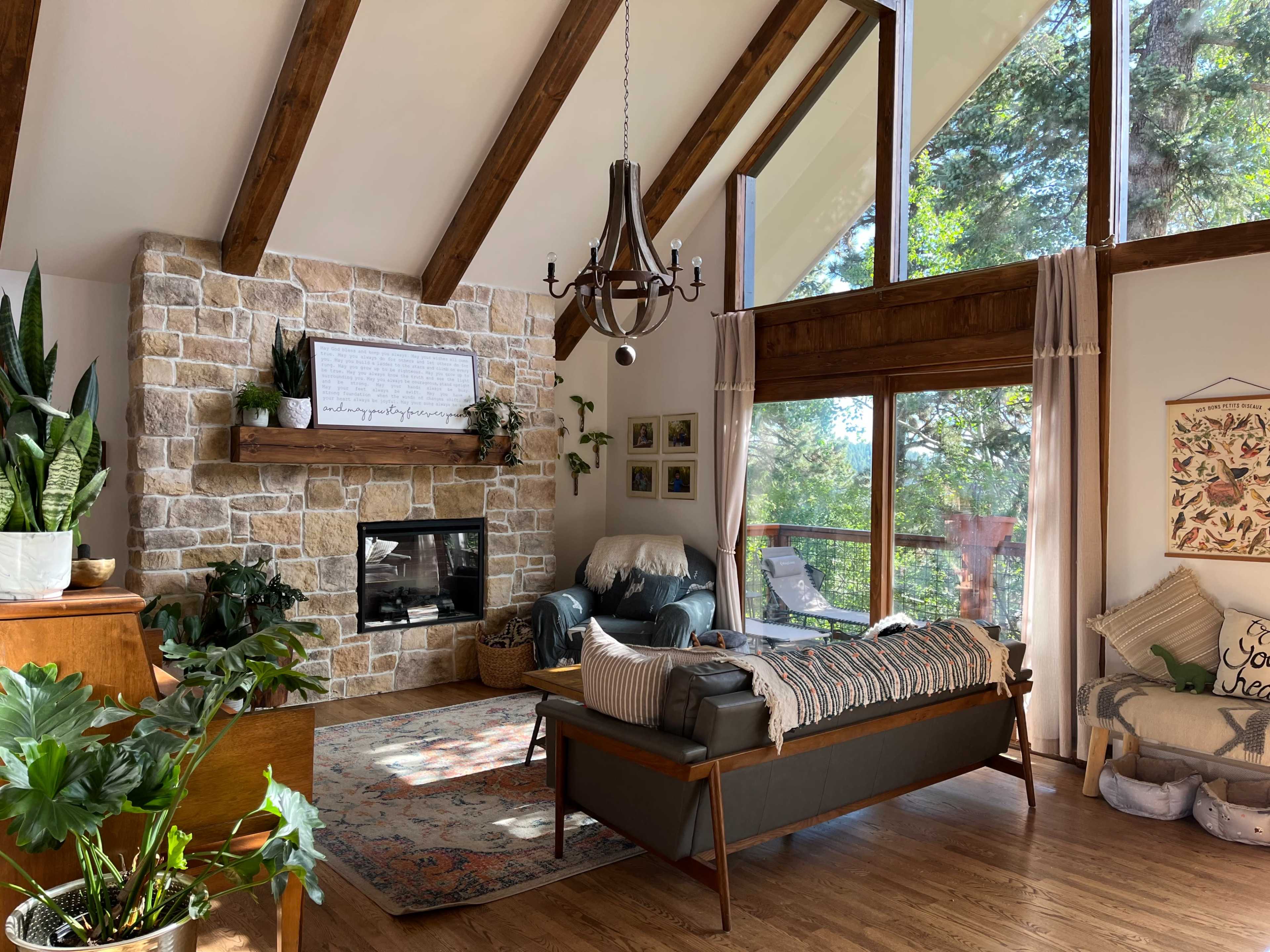 A spacious living room features a stone fireplace, large windows with views of greenery, and comfortable seating options.