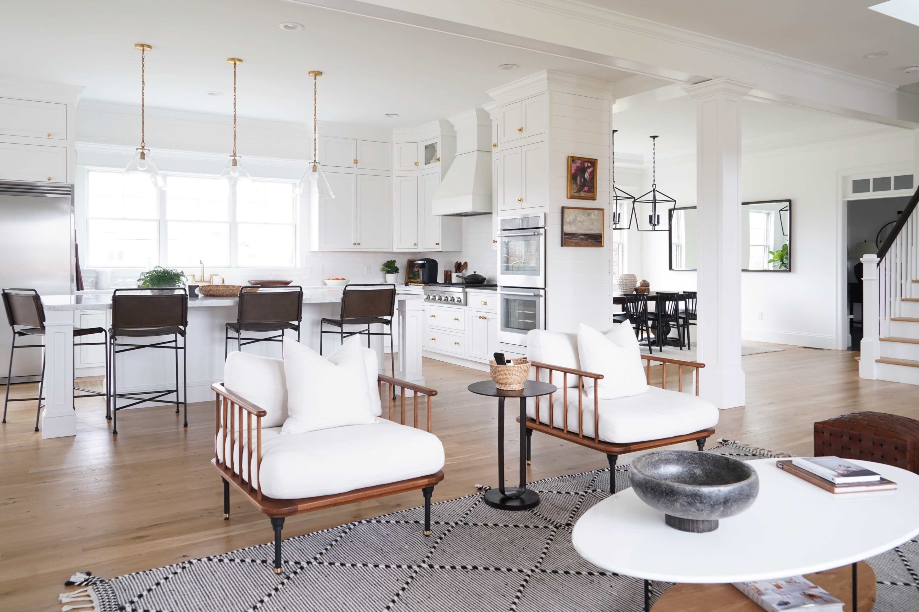A modern open-concept kitchen and living area features white cabinetry, a large island with bar seating, and contemporary furniture arrangements.