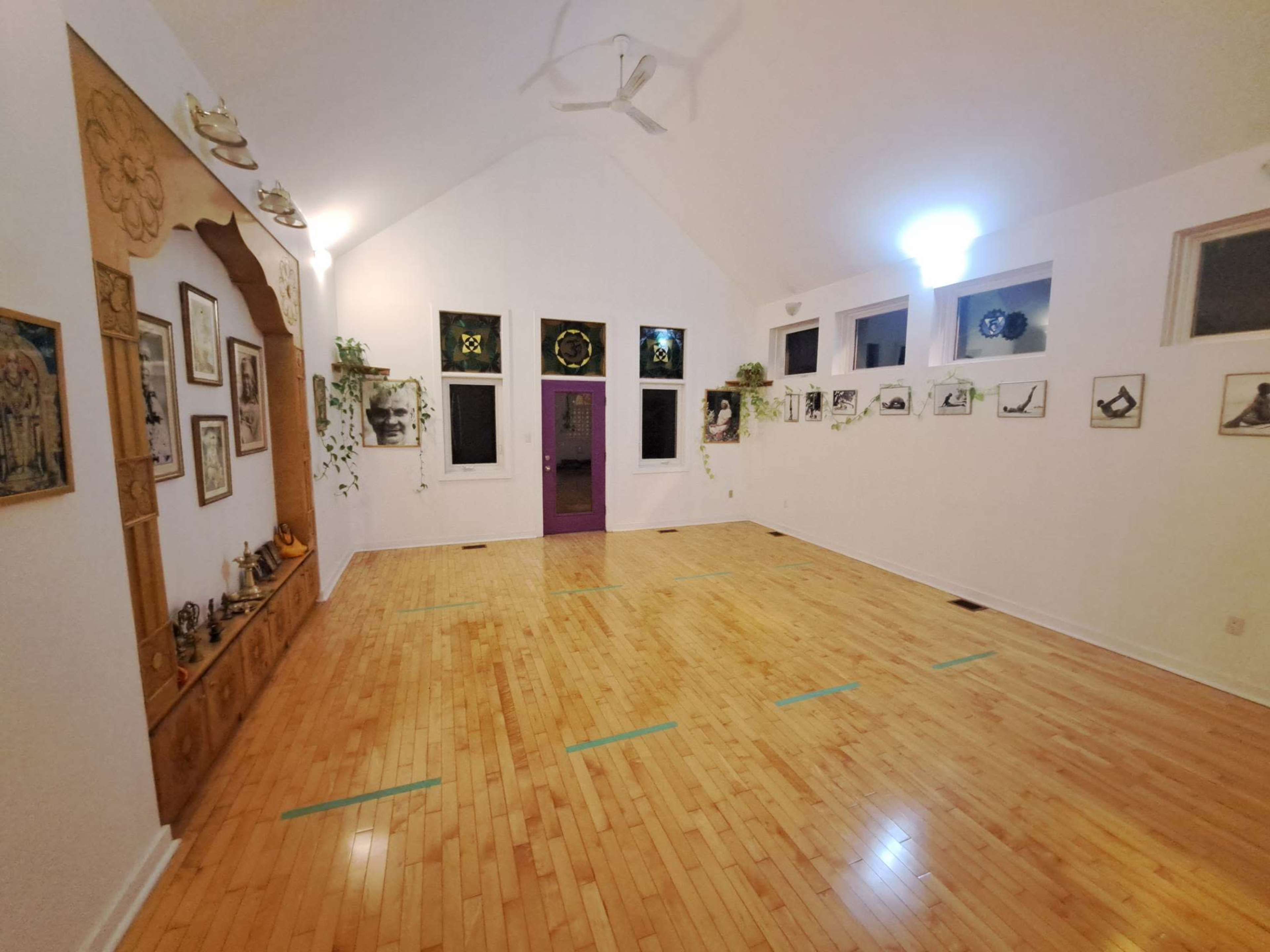 A spacious, empty room with wooden flooring, high ceilings, and a decorative wall shelf adorned with framed pictures and potted plants.