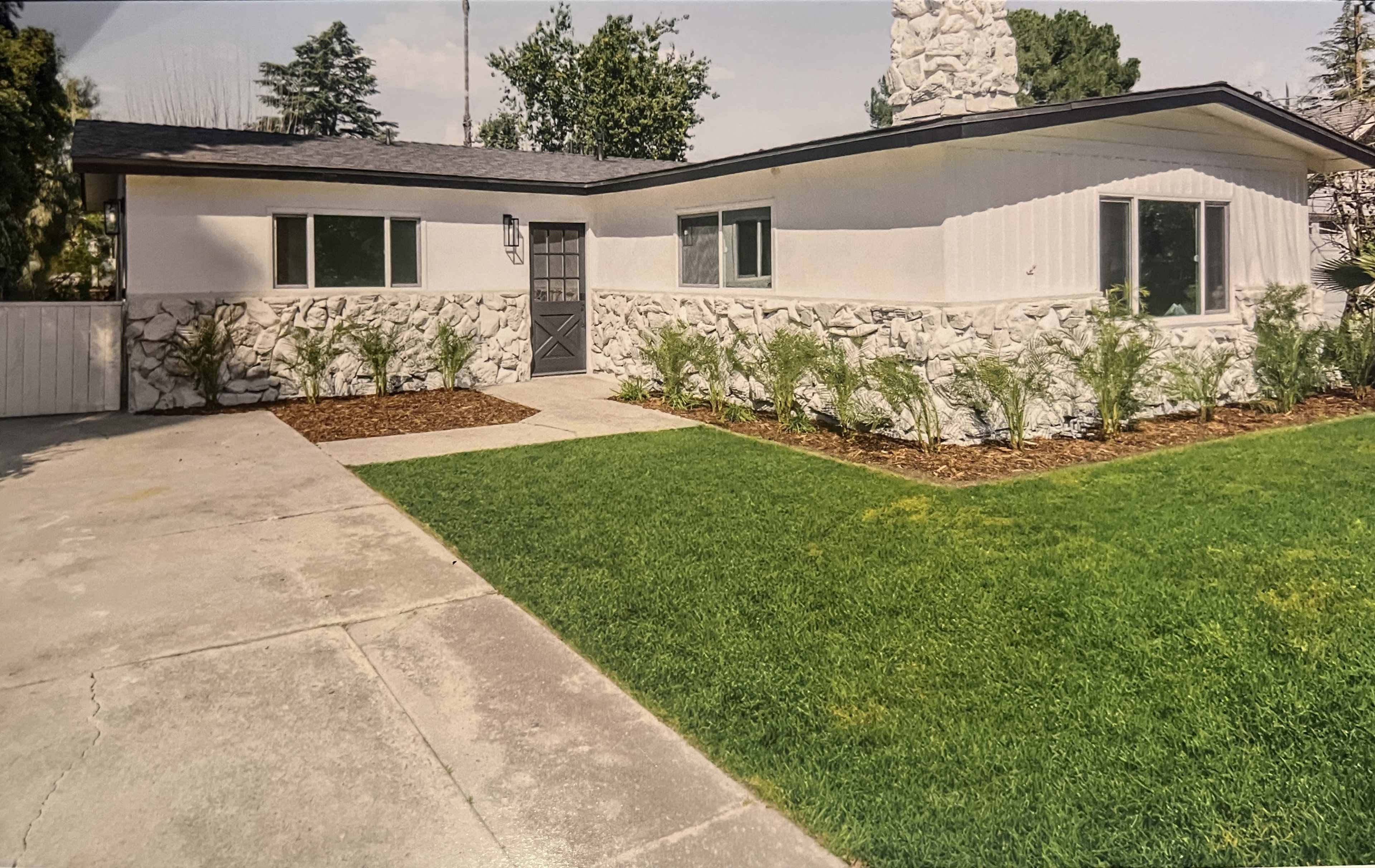The image shows a single-story house with a stone front façade, surrounded by a well-maintained lawn and landscaping.