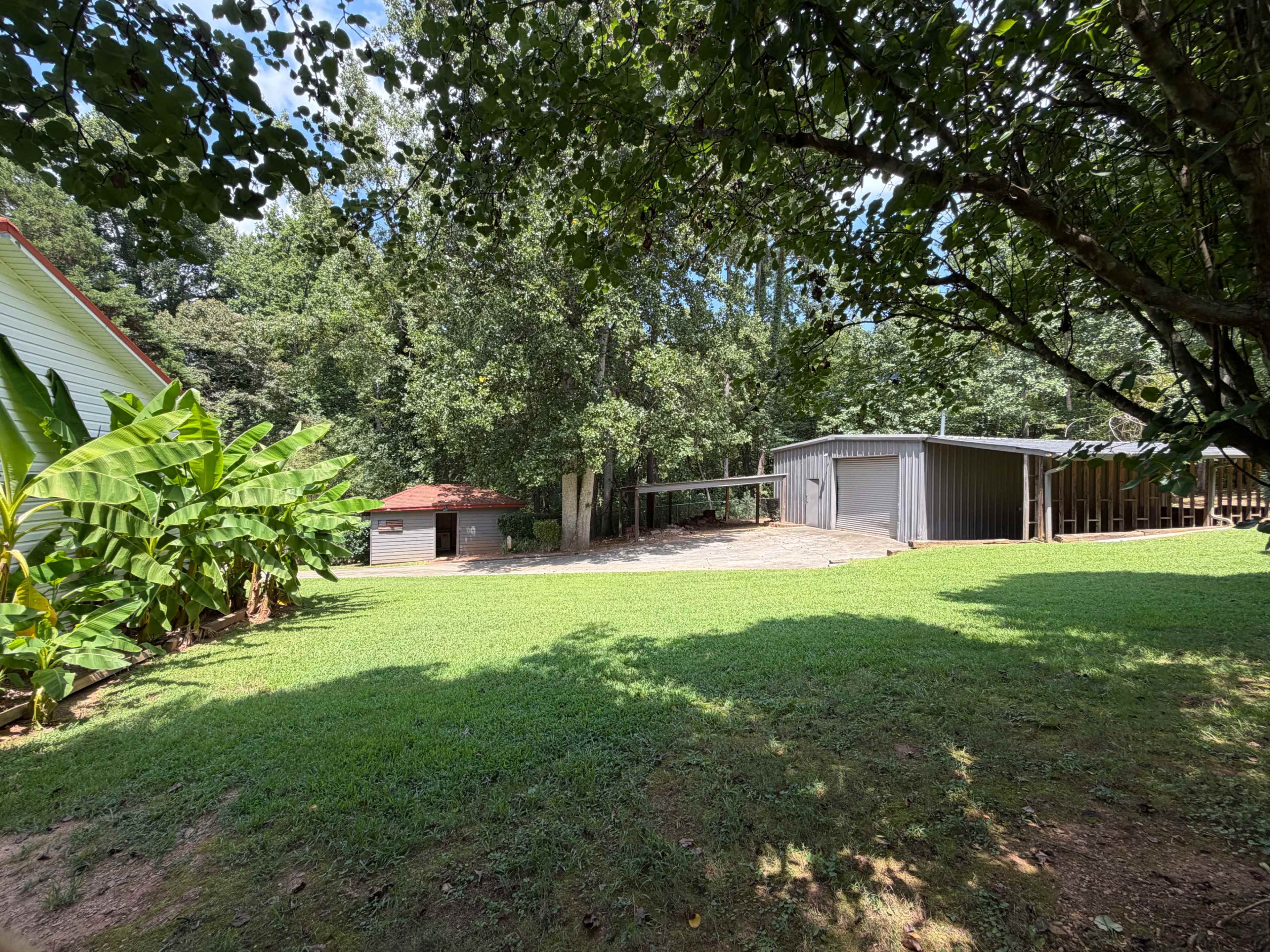 A grassy area features a gazebo and two storage buildings surrounded by trees.