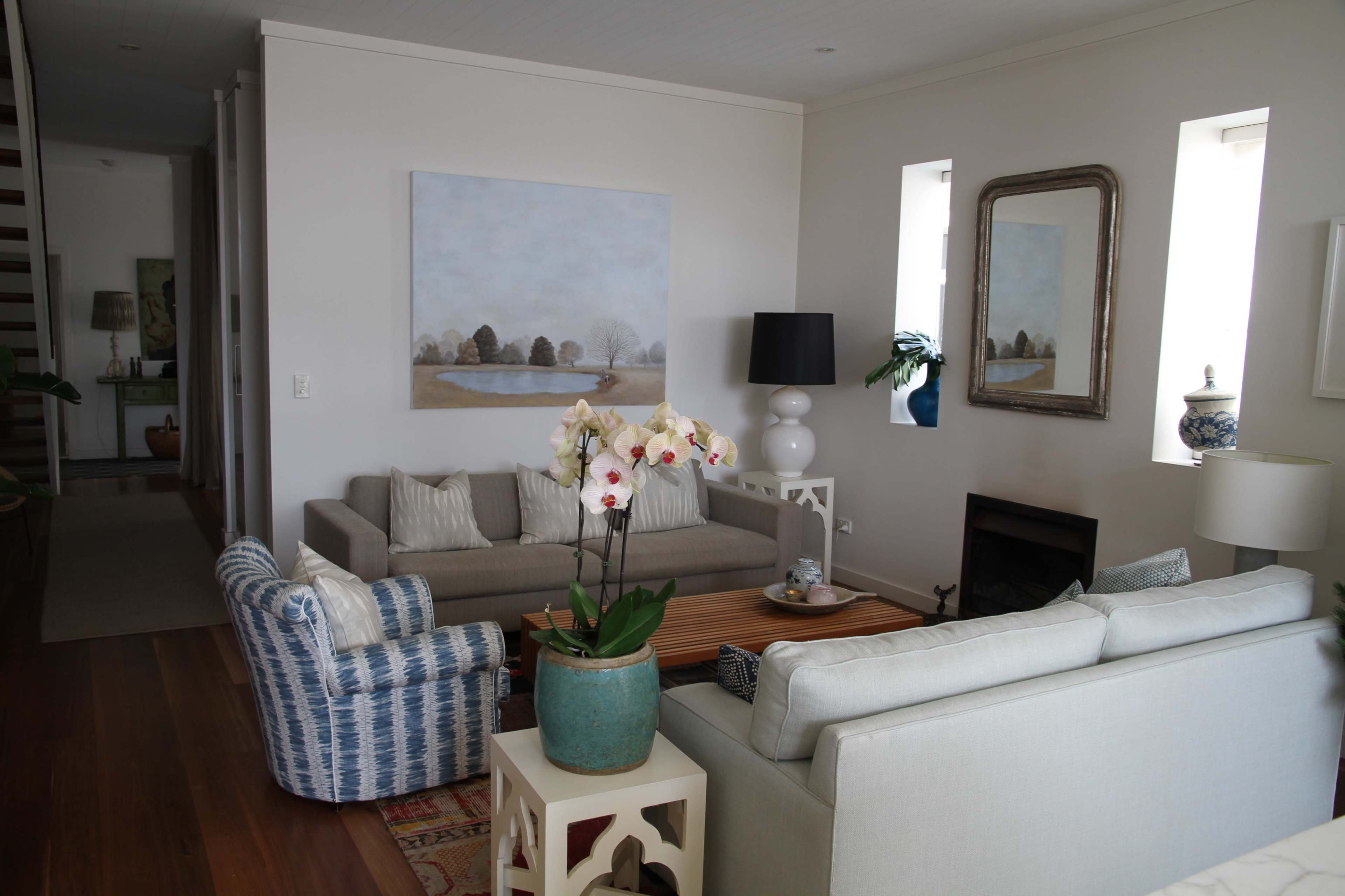 A cozy living room features two sofas, a coffee table, and a large painting, with natural light entering through windows.