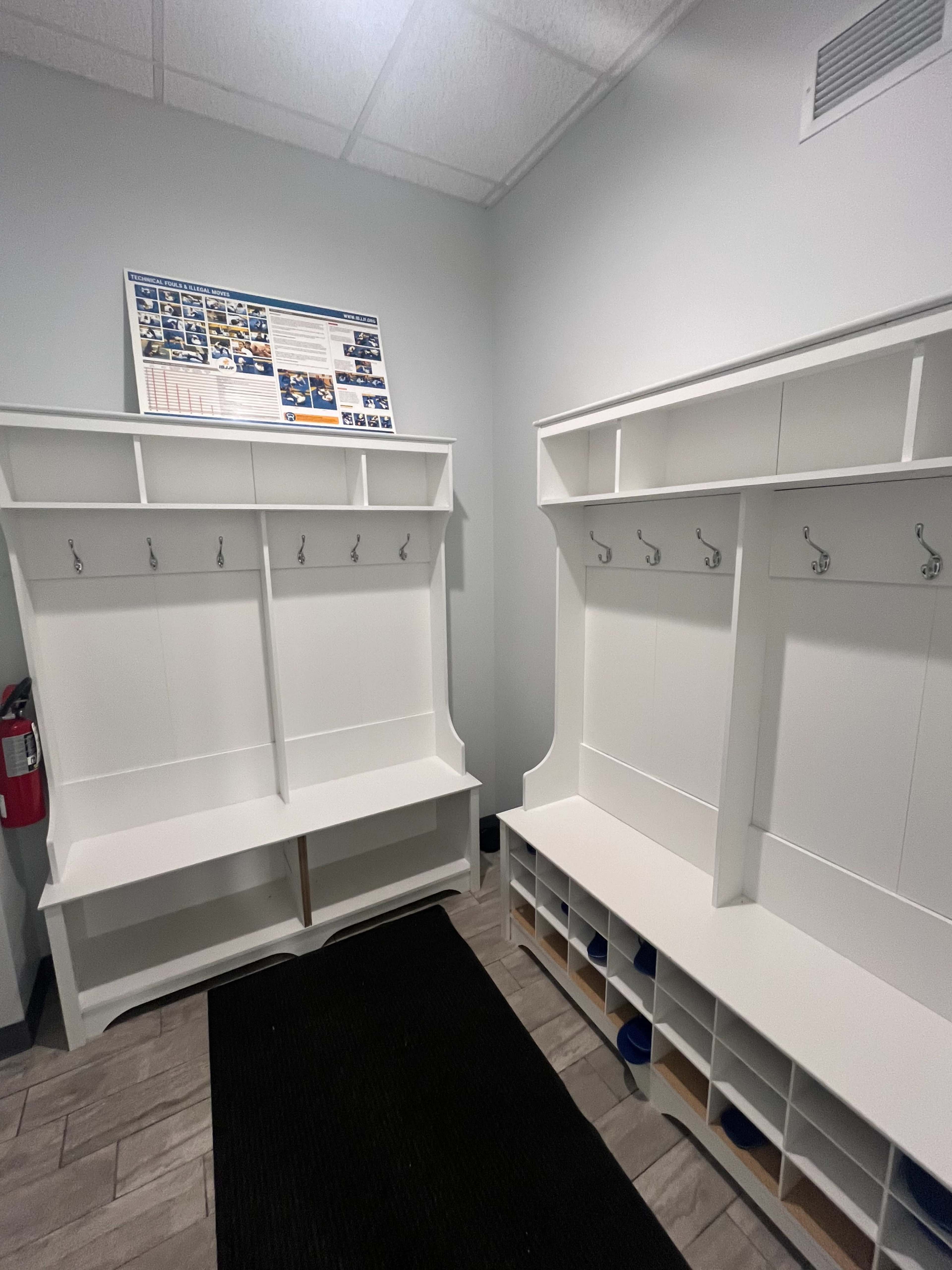 A clean, white locker room with benches and hooks on the wall, along with cubbies for storage.