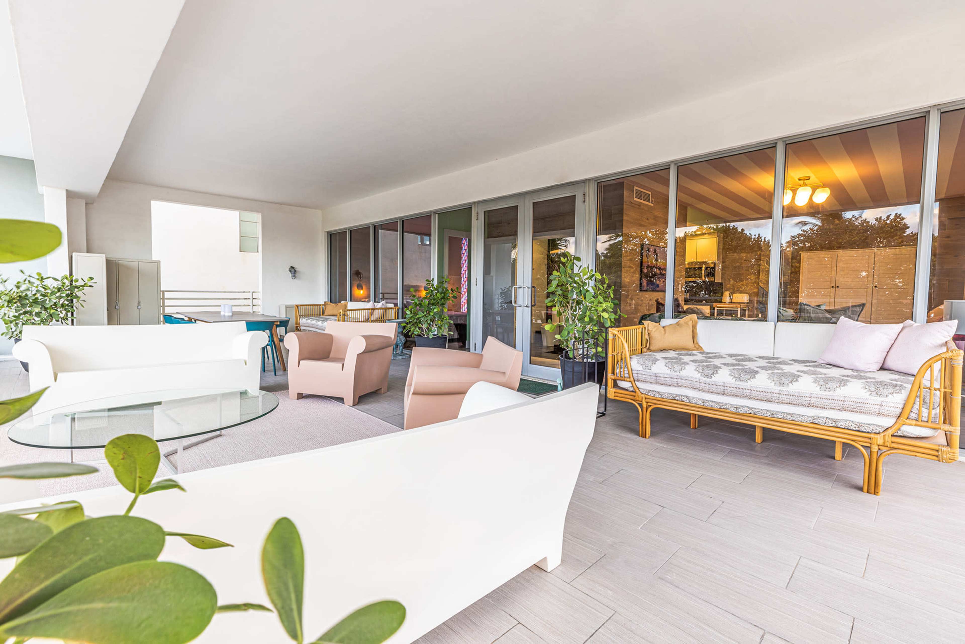 A spacious balcony with modern furniture, including white sofas, a glass table, and potted plants.