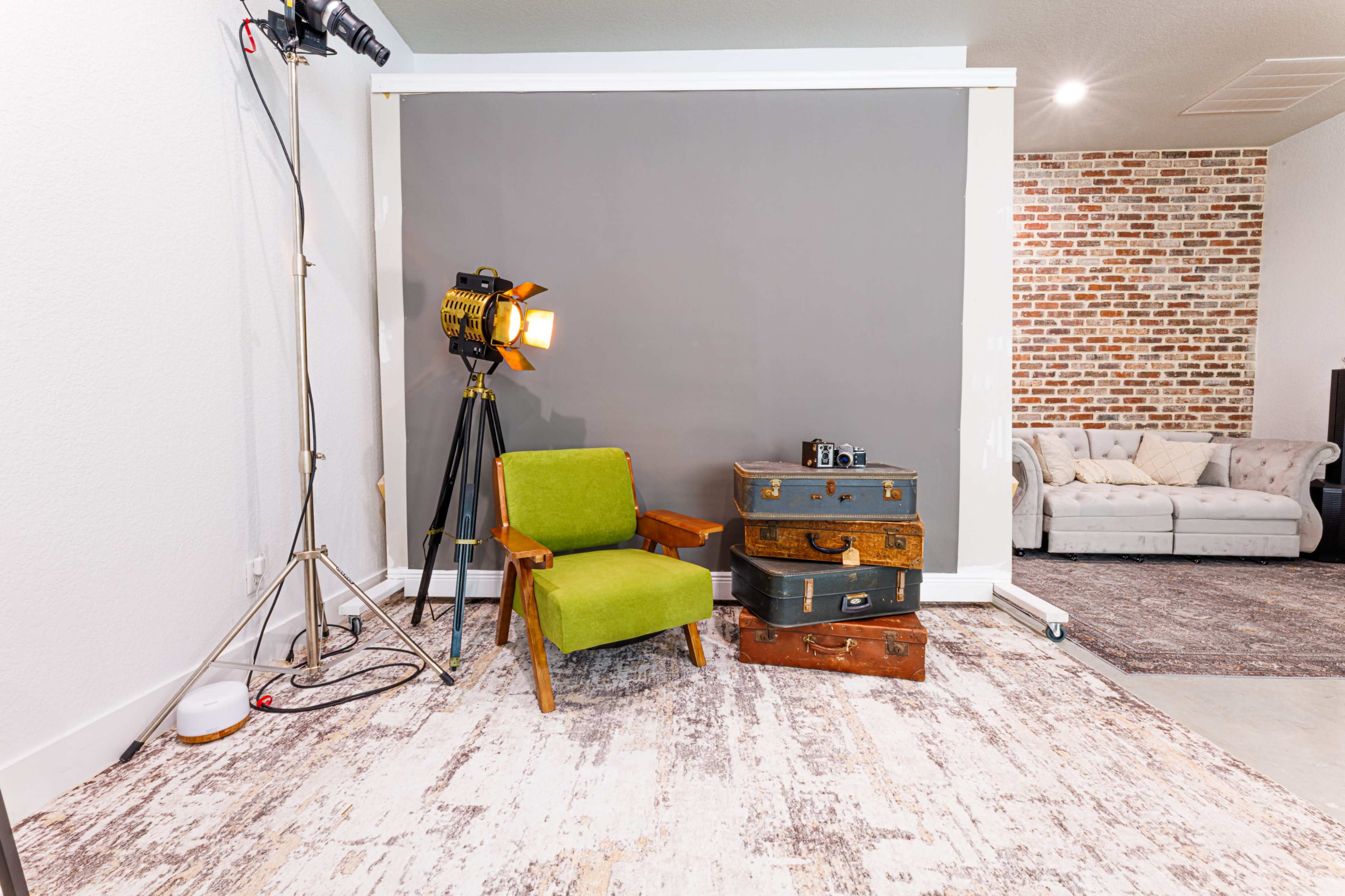 A green chair is positioned next to stacked vintage suitcases in front of a gray backdrop, with a spotlight nearby.