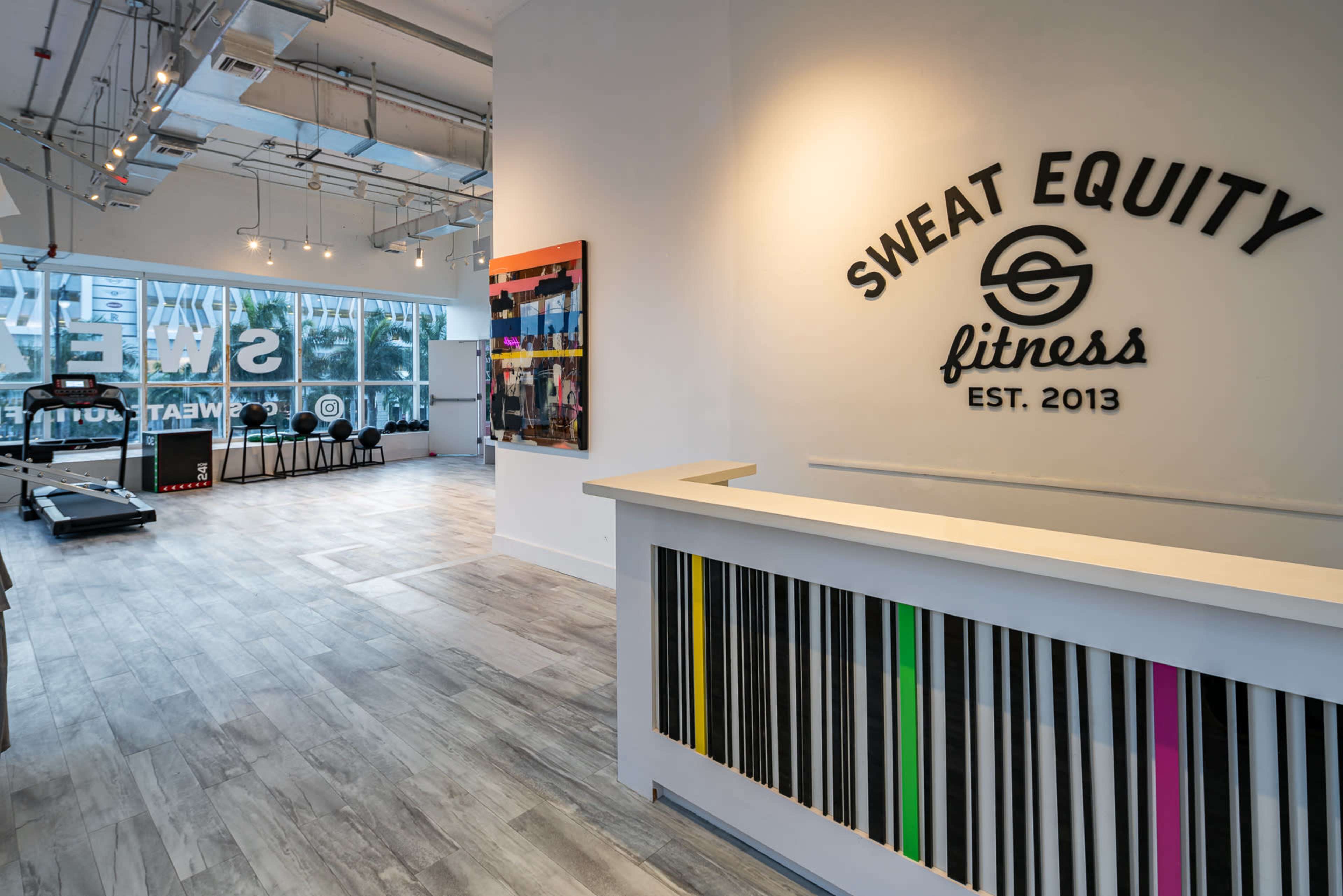 The interior of a fitness studio features a reception area with a branded wall and exercise equipment visible in the background.