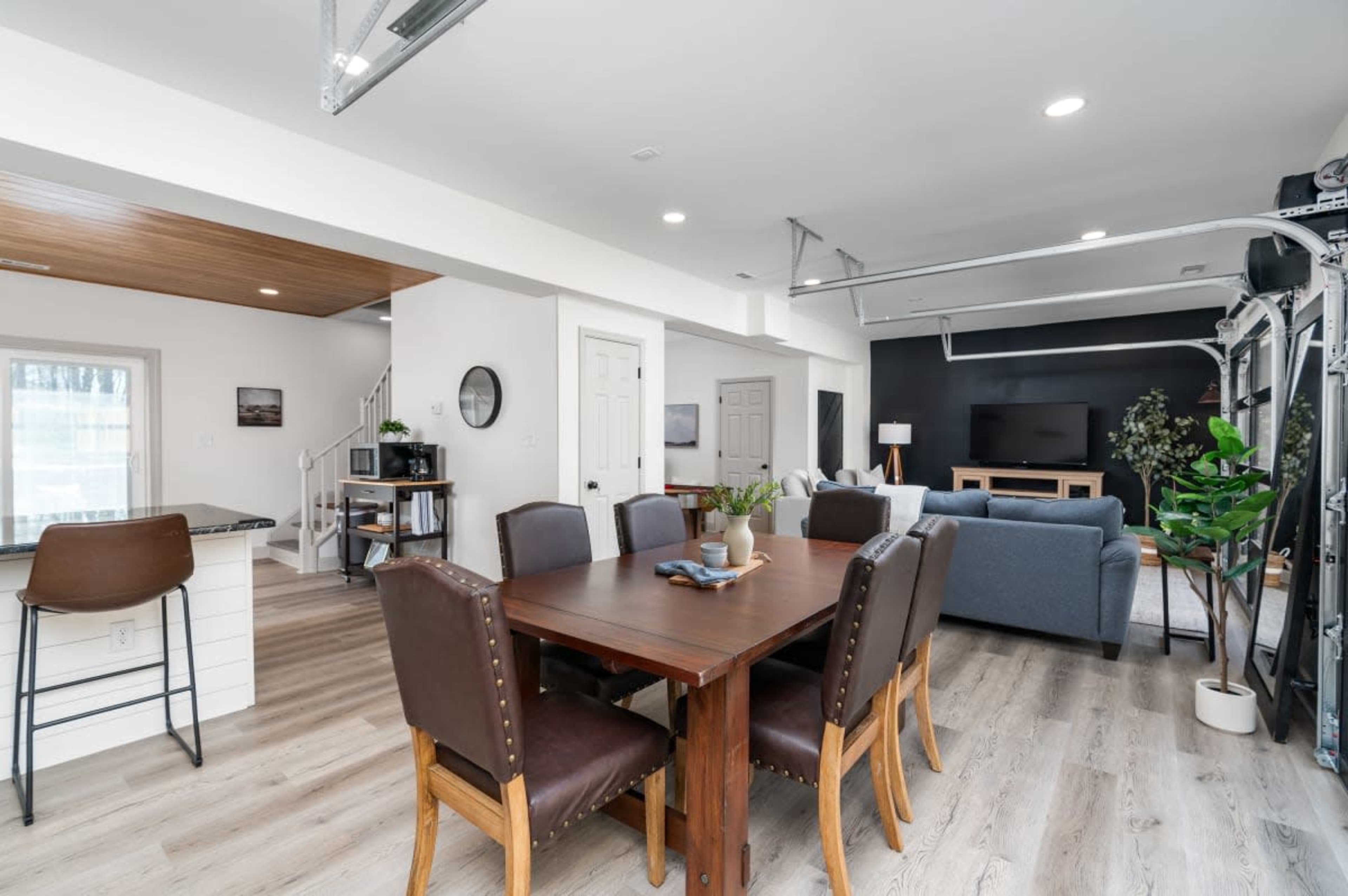 A modern open-concept living and dining area featuring a wooden dining table with brown chairs, a cozy seating arrangement, and large windows allowing natural light.