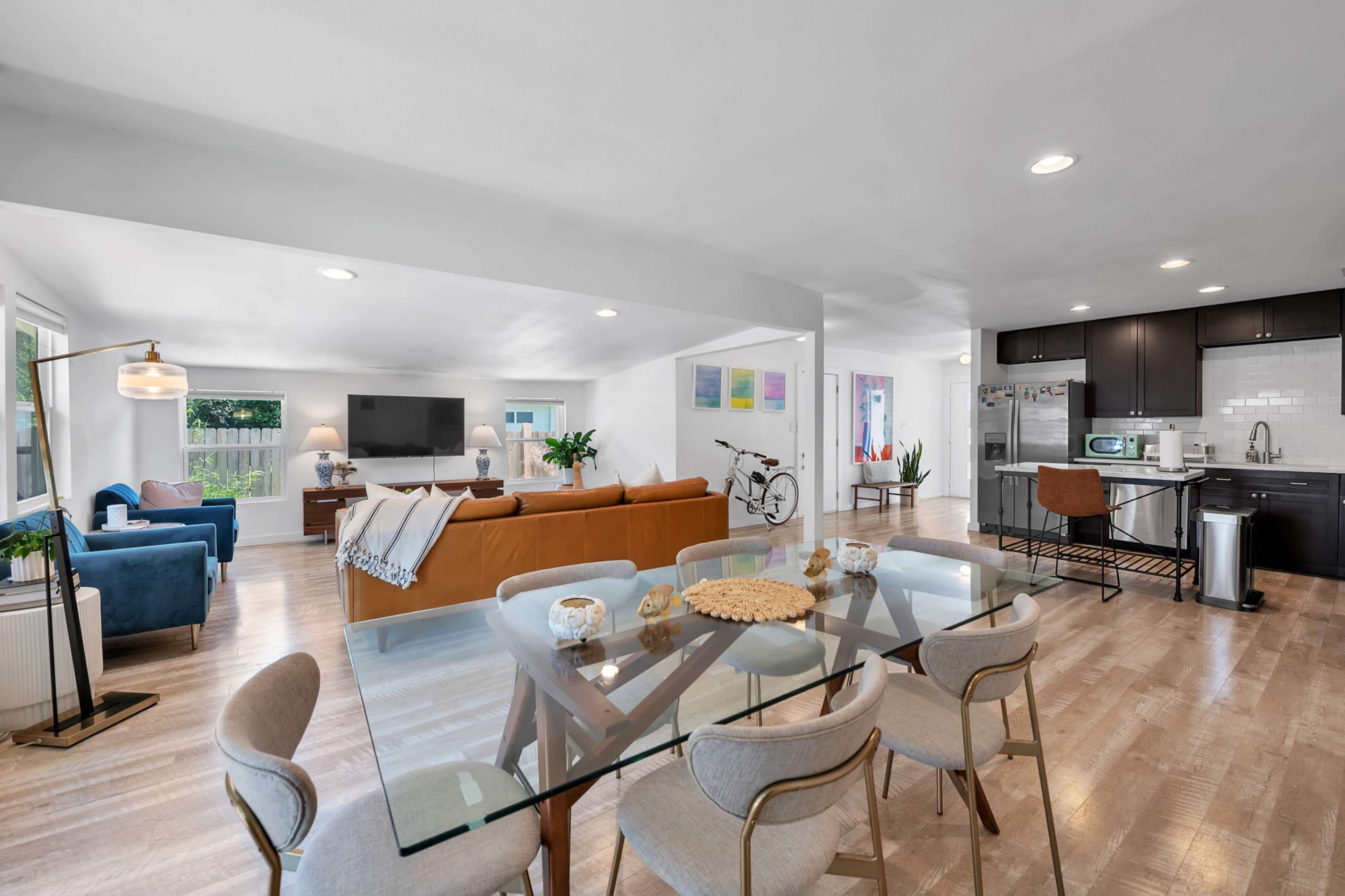 The image shows a modern, open-concept living space with a dining area, kitchen, and seating areas featuring a combination of brown, blue, and neutral furnishings.